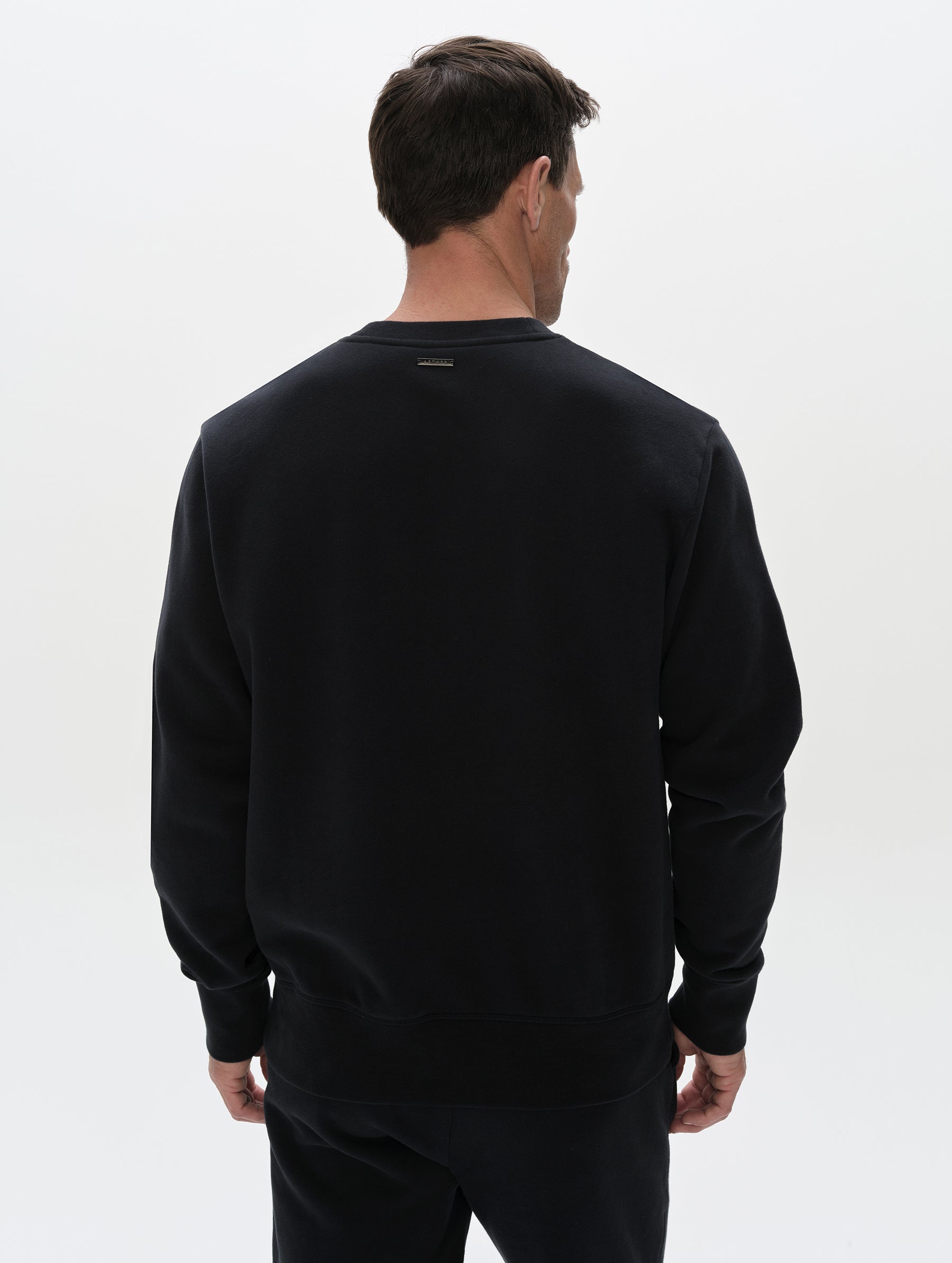 Rear, upper-body view of man wearing the Rylan Crewneck Sweatshirt in Onyx Black from AETHER Apparel.