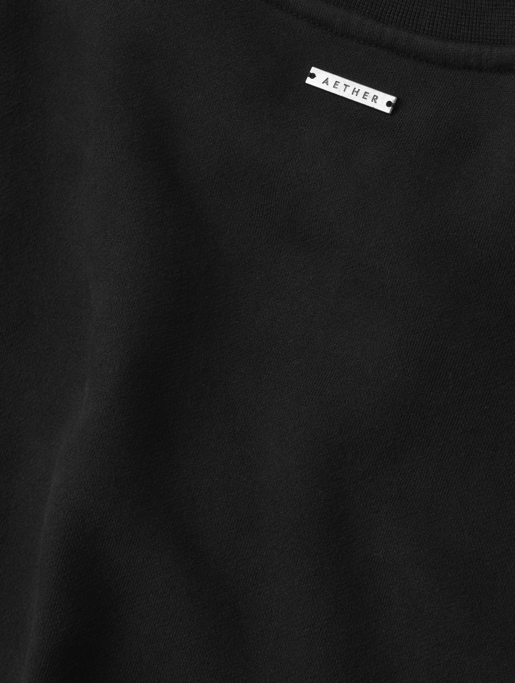 Closeup detailed view of the fabric and metal logo plate on the Rylan Crewneck Sweatshirt in Onyx Black from AETHER Apparel.