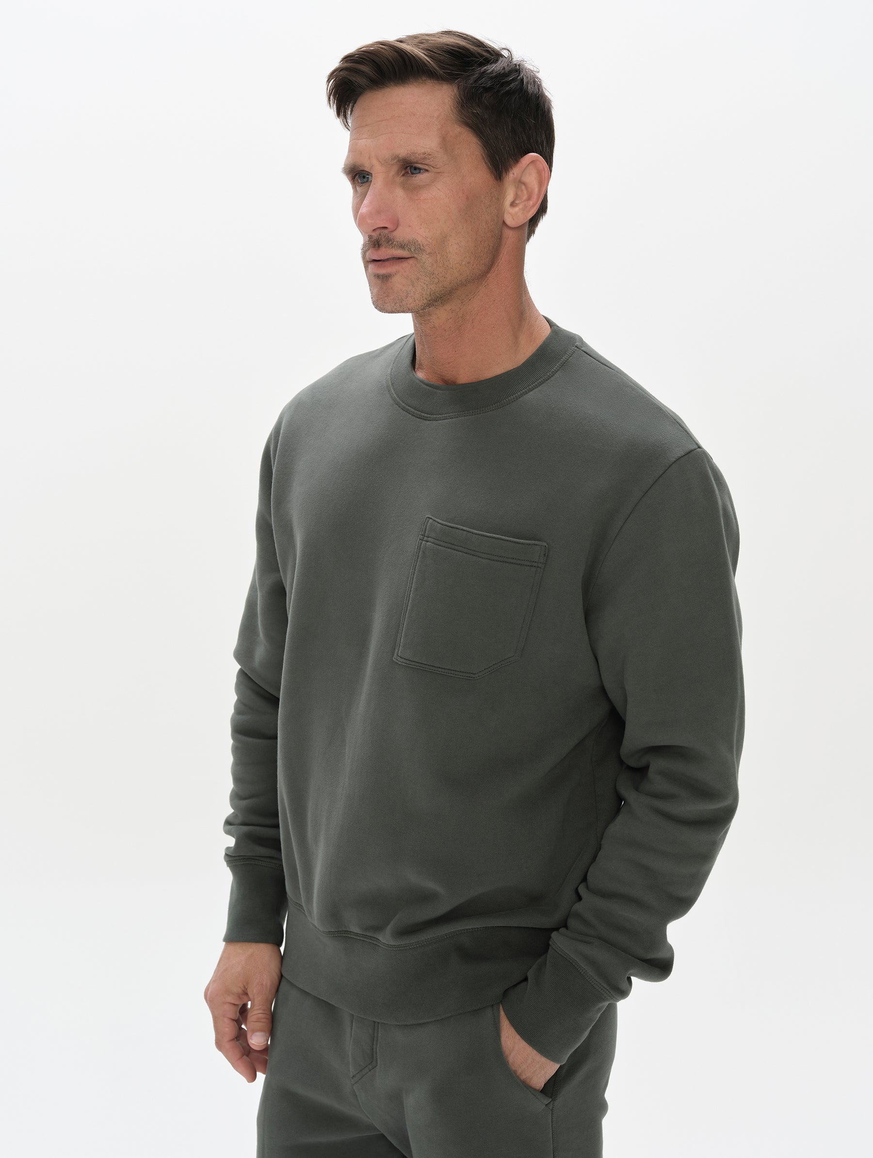 Front, 3/4, upper-body view of man wearing the Rylan Crewneck Sweatshirt in Saville Green from AETHER Apparel.