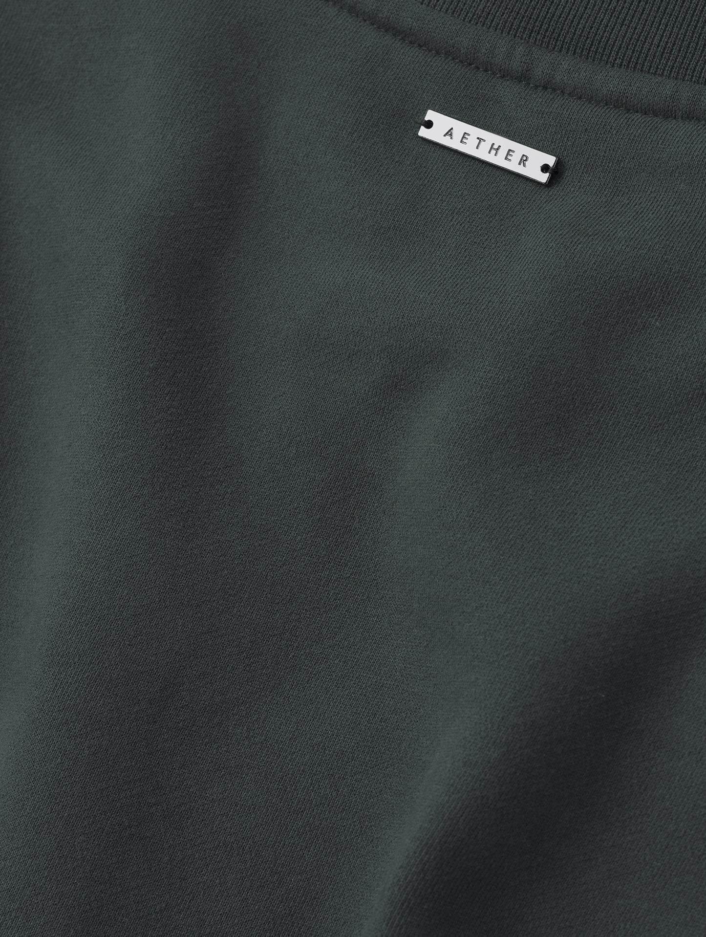 Closeup detailed view of the fabric and metal logo plate on the Rylan Crewneck Sweatshirt in Saville Green from AETHER Apparel.