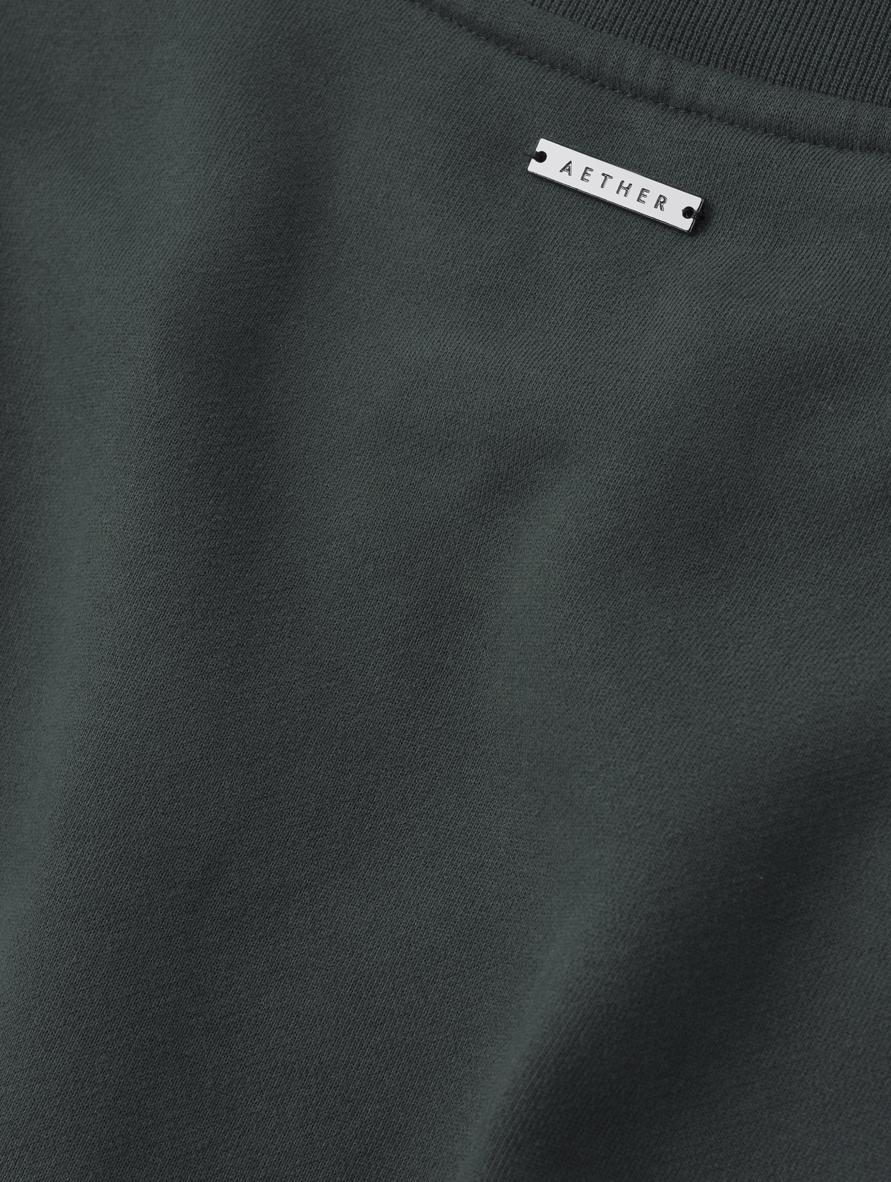 Closeup detailed view of the fabric and metal logo plate on the Rylan Crewneck Sweatshirt in Saville Green from AETHER Apparel.