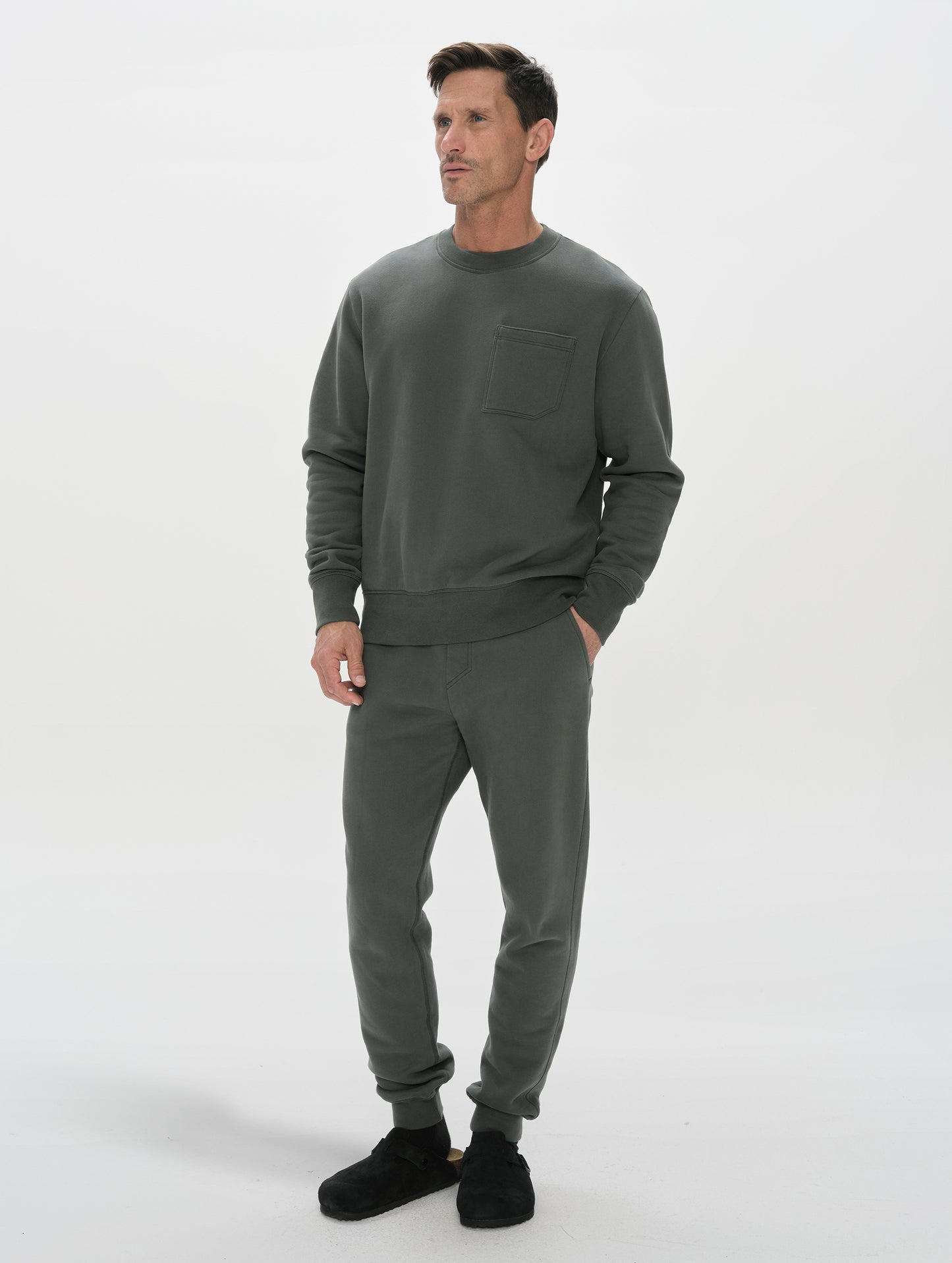 Front, 3/4, full-body view of man wearing the Rylan Crewneck Sweatshirt in Saville Green from AETHER Apparel.