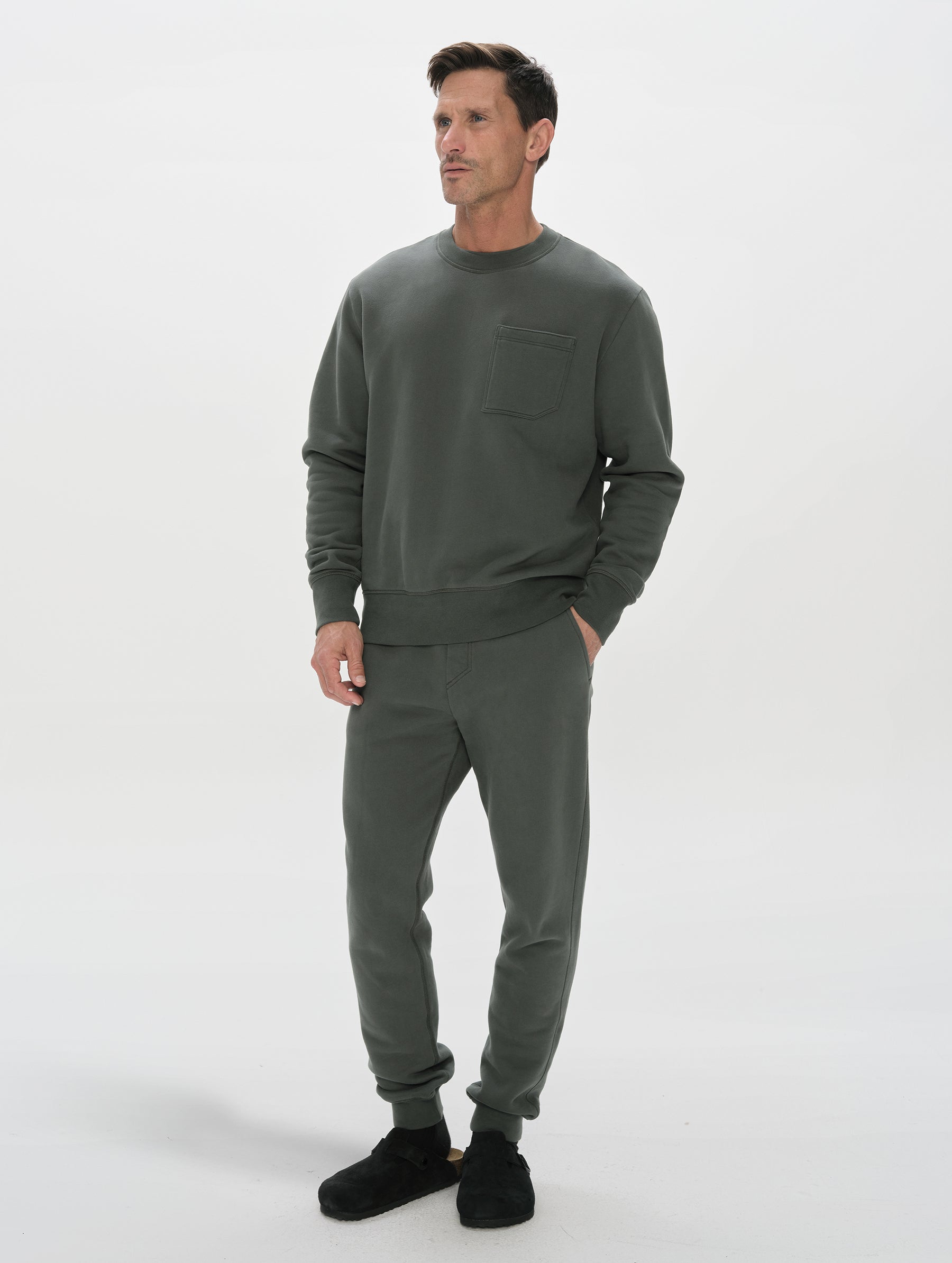 Front, 3/4, full-body view of man wearing the Rylan Crewneck Sweatshirt in Saville Green from AETHER Apparel.