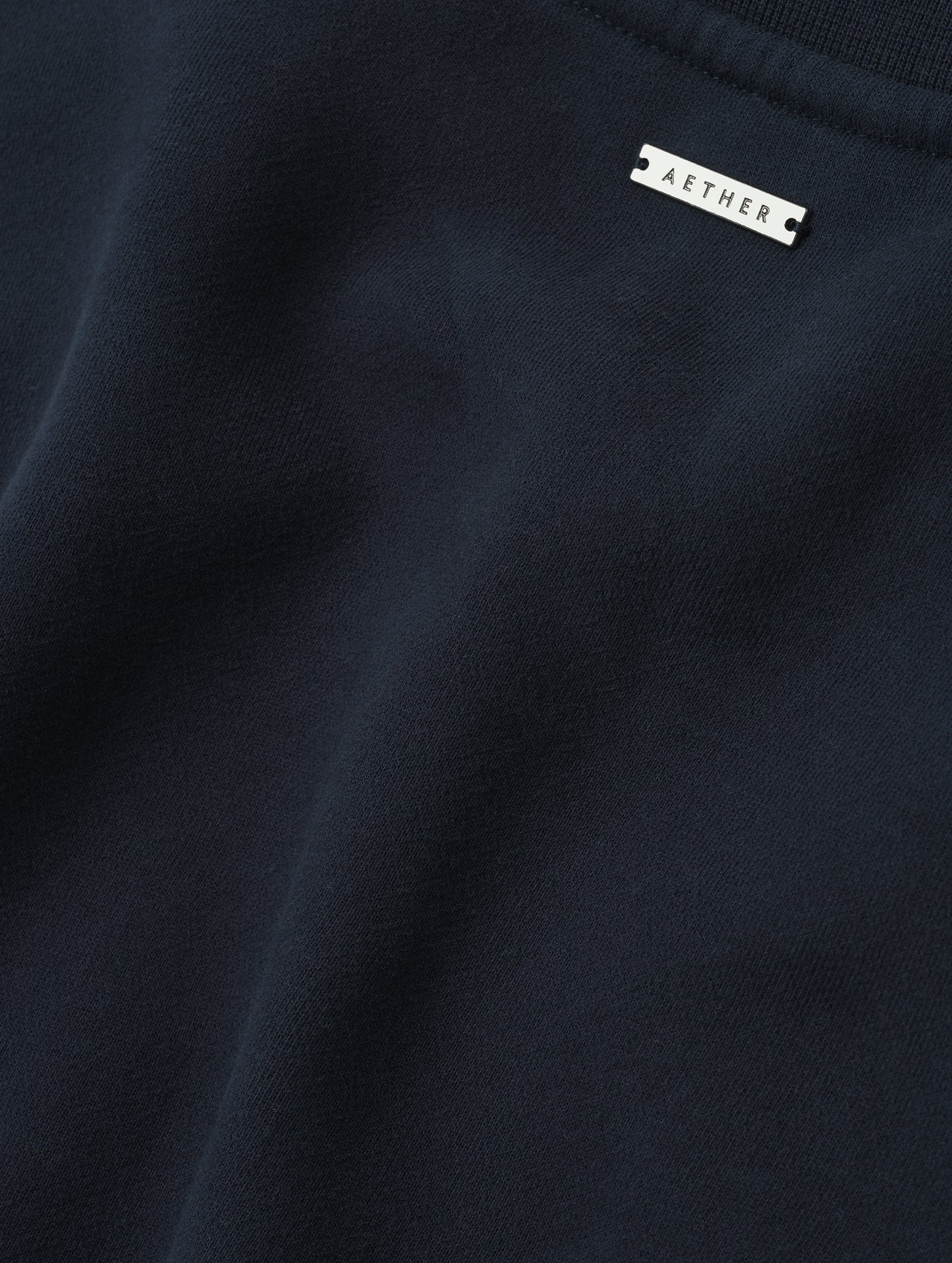 Closeup detailed view of the metal logo plate on the Rylan Crewneck Sweatshirt in Total Eclipse from AETHER Apparel.