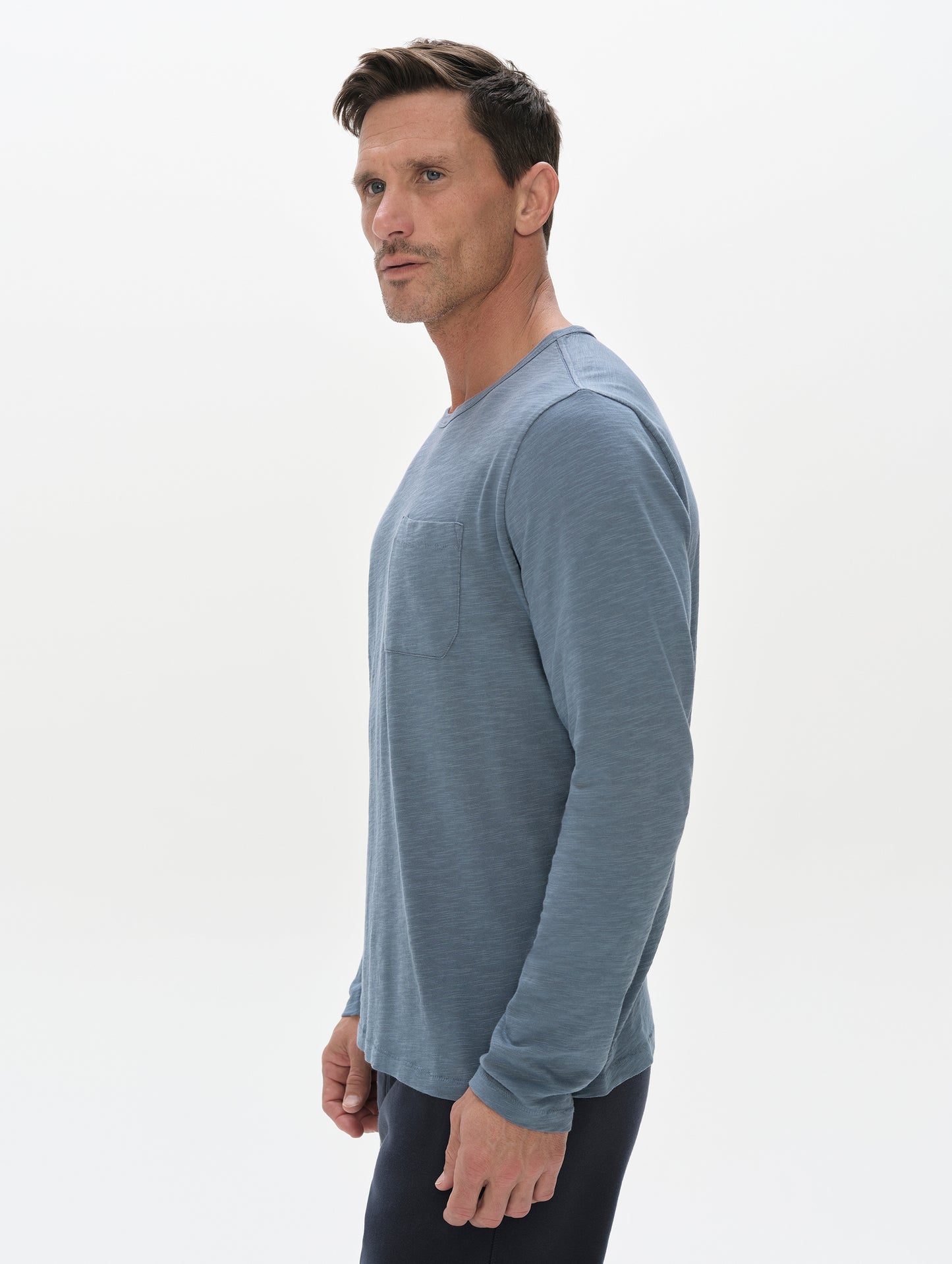 Side profile, upper-body view of man wearing the Slub Pocket Long-Sleeve Tee 2.0 in Portal Blue from AETHER Apparel.