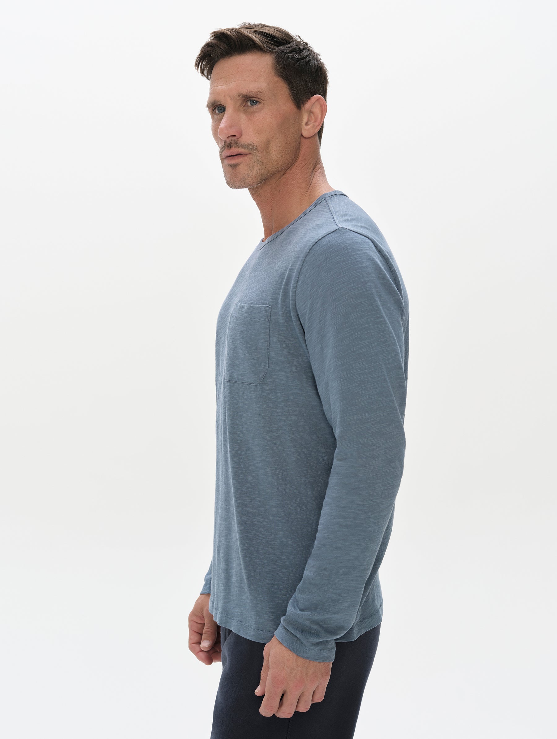 Side profile, upper-body view of man wearing the Slub Pocket Long-Sleeve Tee 2.0 in Portal Blue from AETHER Apparel.