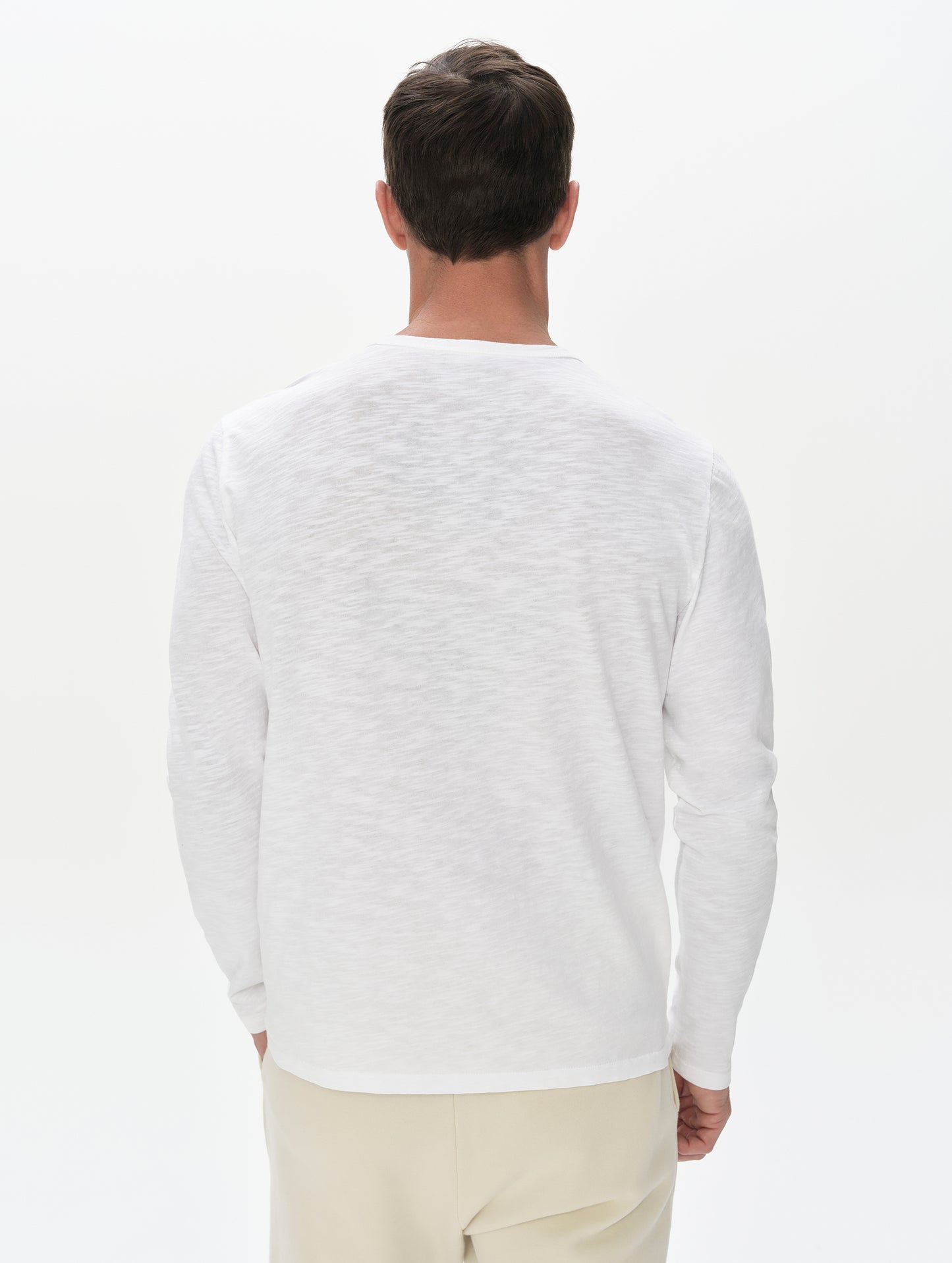 Rear, upper-body view of man wearing Slub Long-Sleeve Pocket Tee 2.0 in White from AETHER Apparel.