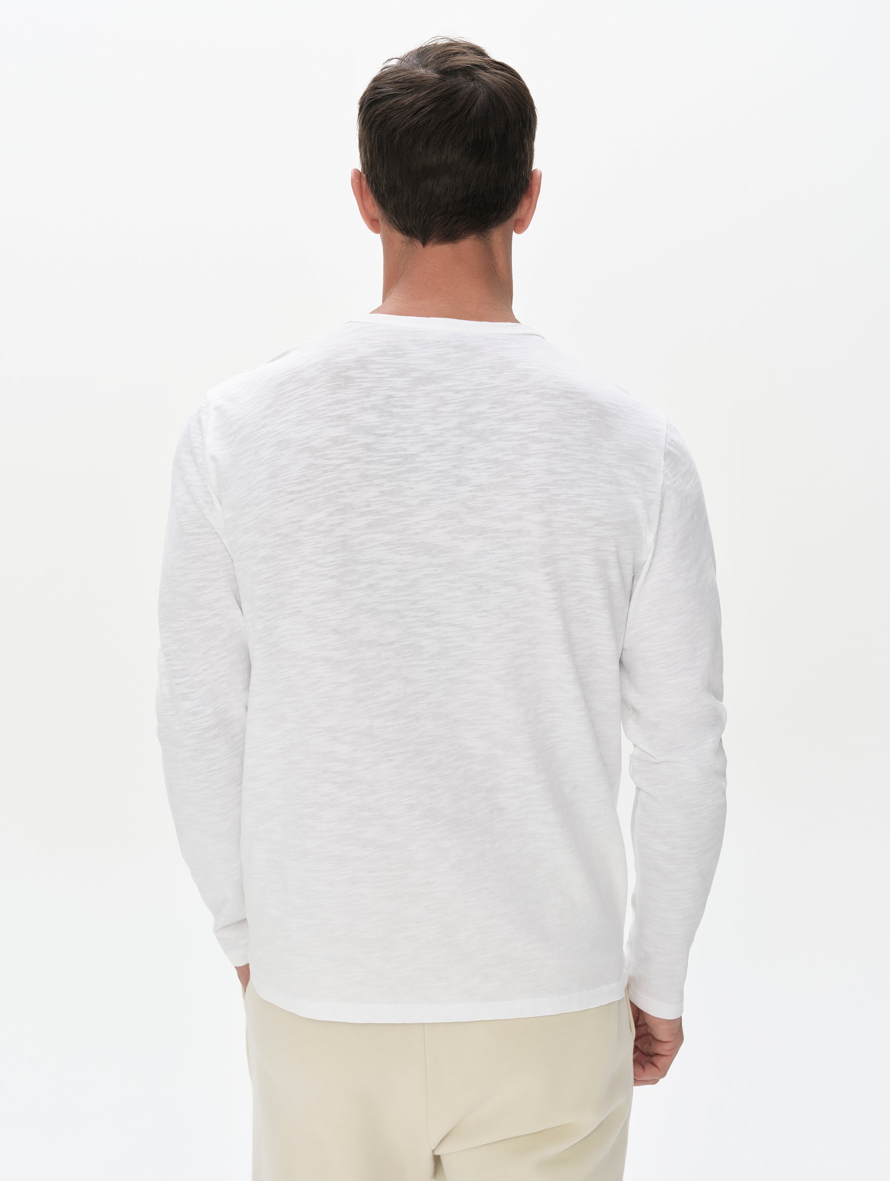 Rear, upper-body view of man wearing Slub Long-Sleeve Pocket Tee 2.0 in White from AETHER Apparel.