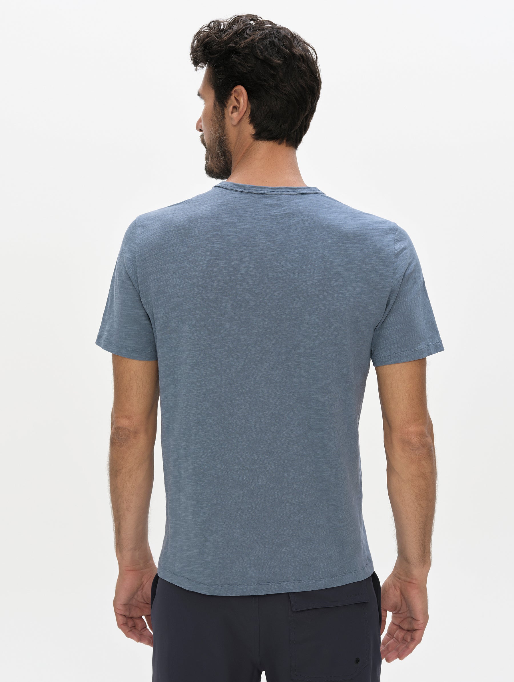 Rear, upper-body view of man wearing the Slub Pocket Tee 2.0 in Portal Blue from AETHER Apparel.
