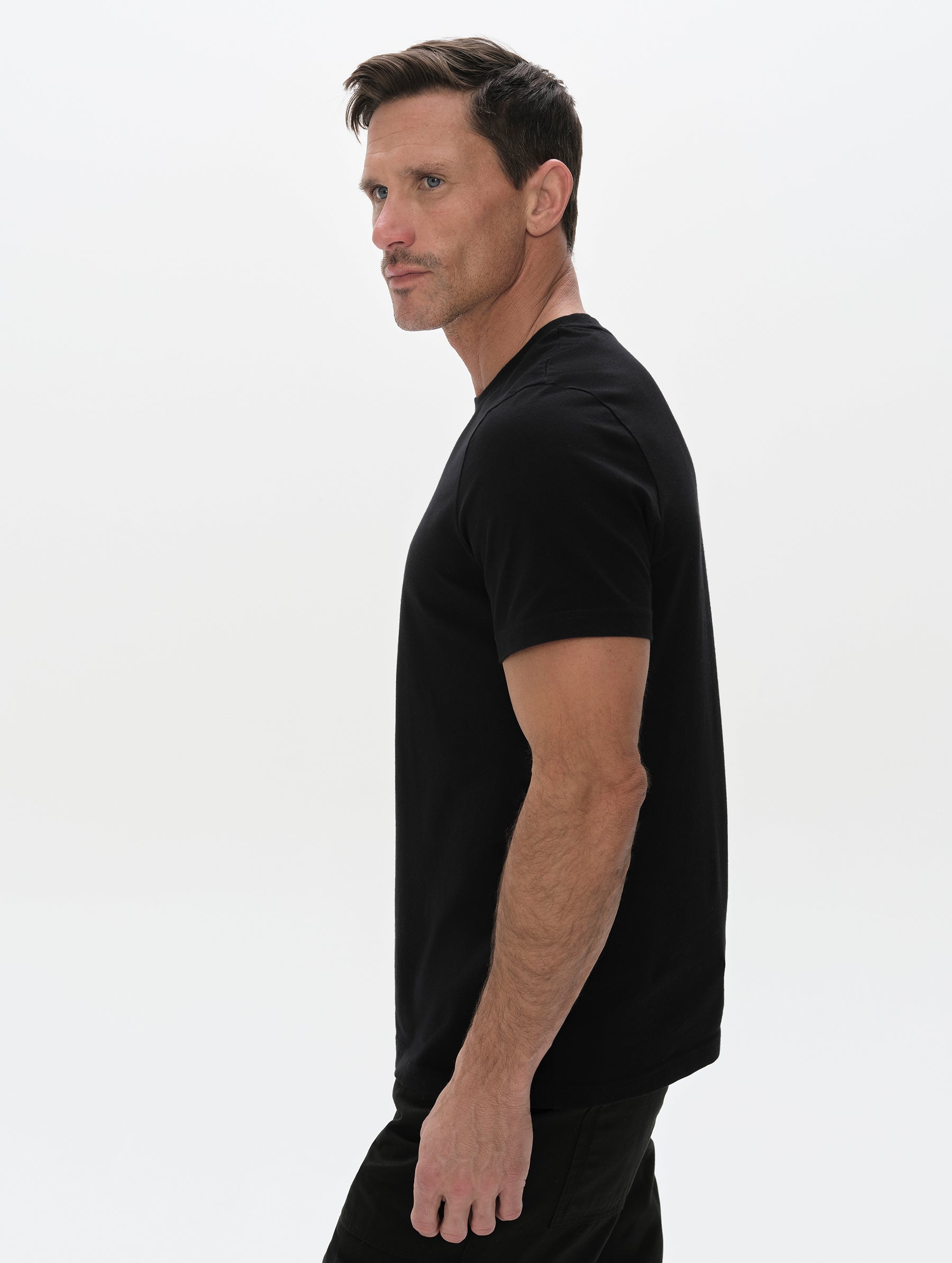 Side profile, upper-body view of man wearing the Standard Tee in Onyx Black from AETHER Apparel.