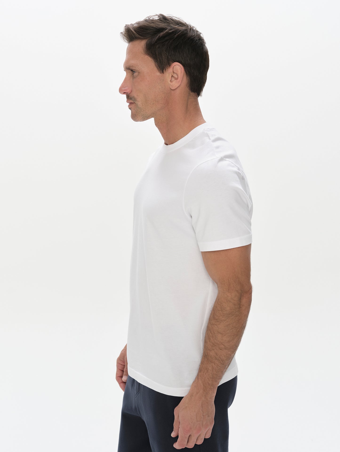 Side profile, upper-body view of man wearing the Standard Tee in White from AETHER Apparel.