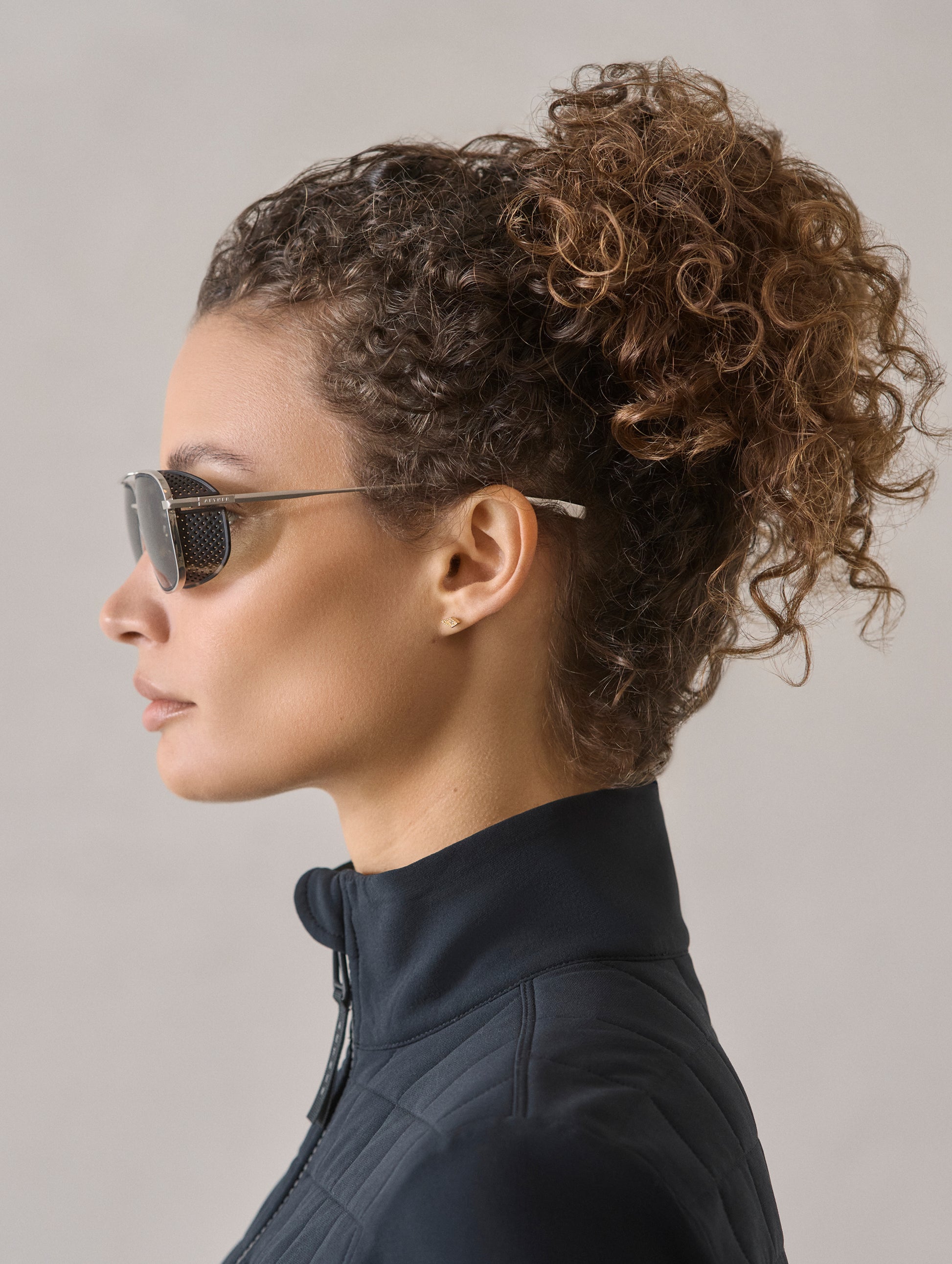 Side profile view of woman wearing Summit Sunglass in Brushed Silver titanium with Grey Lens from AETHER Apparel.