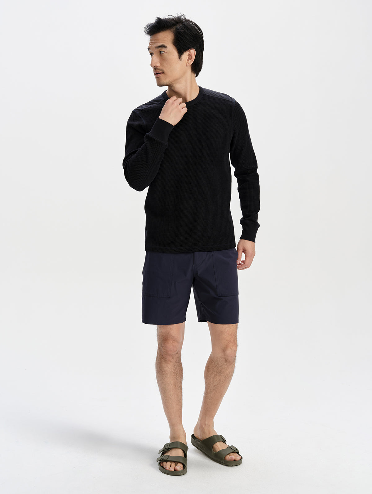 Full-length view of a model in the Velo Short in Total Eclipse with a black crewneck sweater and sandals.