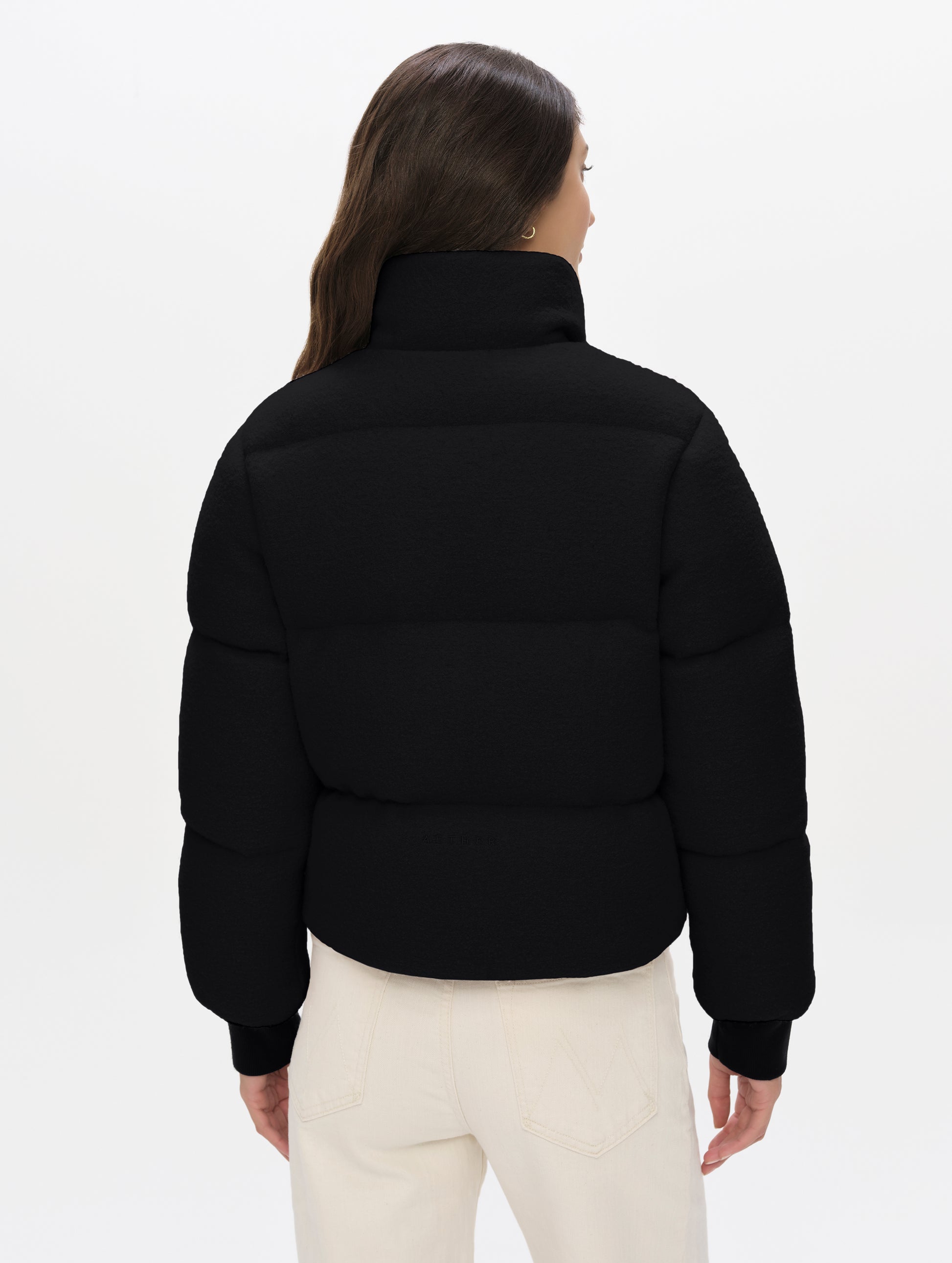 Rear angled upper-body view of woman wearing the Aura Puffer Jacket Wool in Onyx Black from AETHER Apparel.