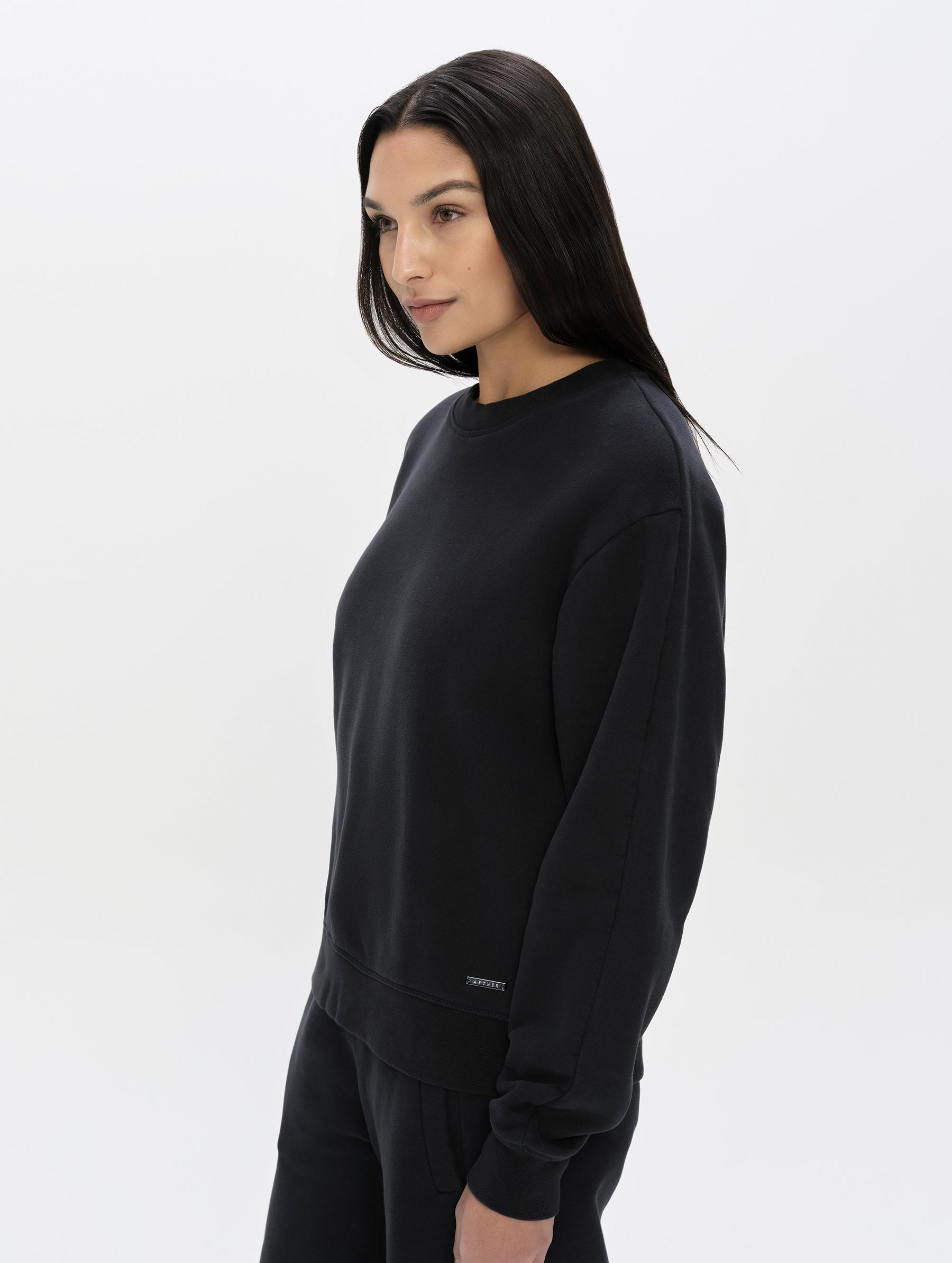 Side profile, upper-body view of woman wearing the Ayla Crewneck Sweatshirt in Onyx Black from AETHER Apparel.