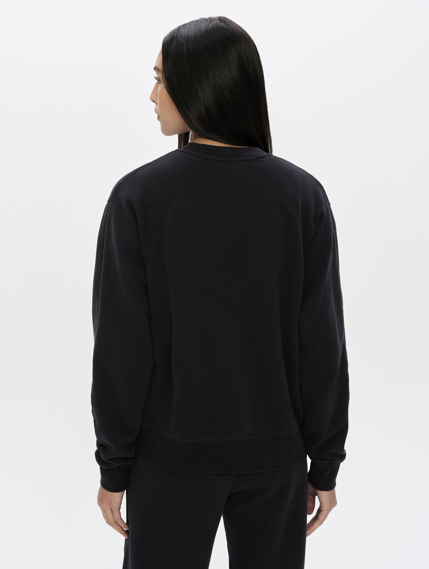 Rear, upper-body view of woman wearing the Ayla Crewneck Sweatshirt in Onyx Black from AETHER Apparel.