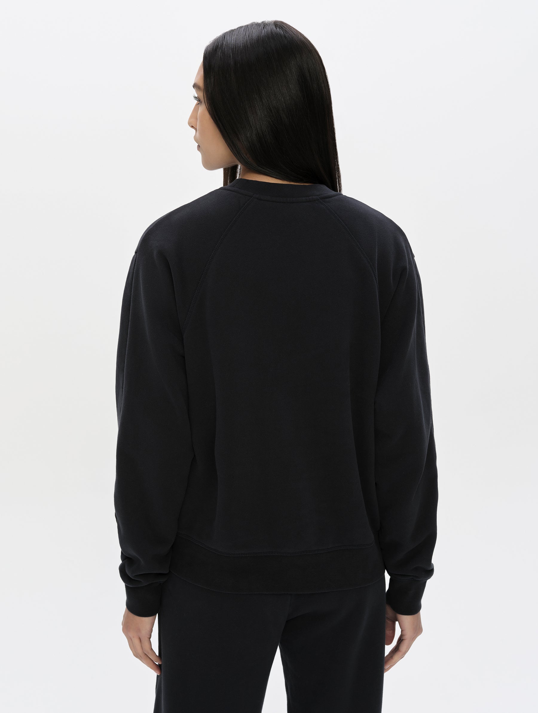 Rear, upper-body view of woman wearing the Ayla Crewneck Sweatshirt in Onyx Black from AETHER Apparel.