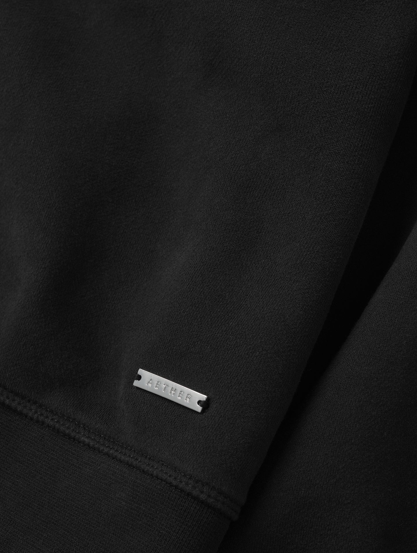 Closeup detailed view of the metal logo plate on the Ayla Crewneck Sweatshirt in Onyx Black from AETHER Apparel.
