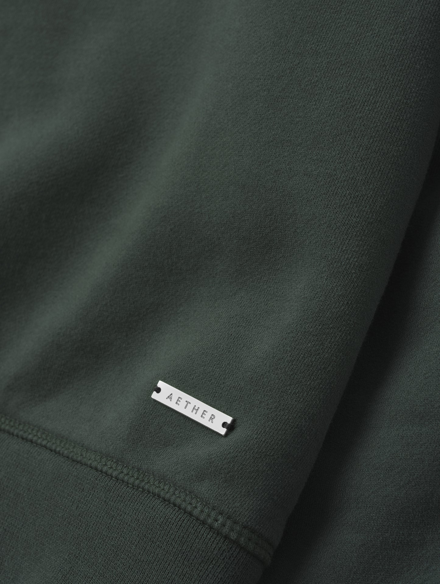 Closeup detailed view of the metal logo plate on the Ayla Crewneck Sweatshirt in Saville Green from AETHER Apparel.