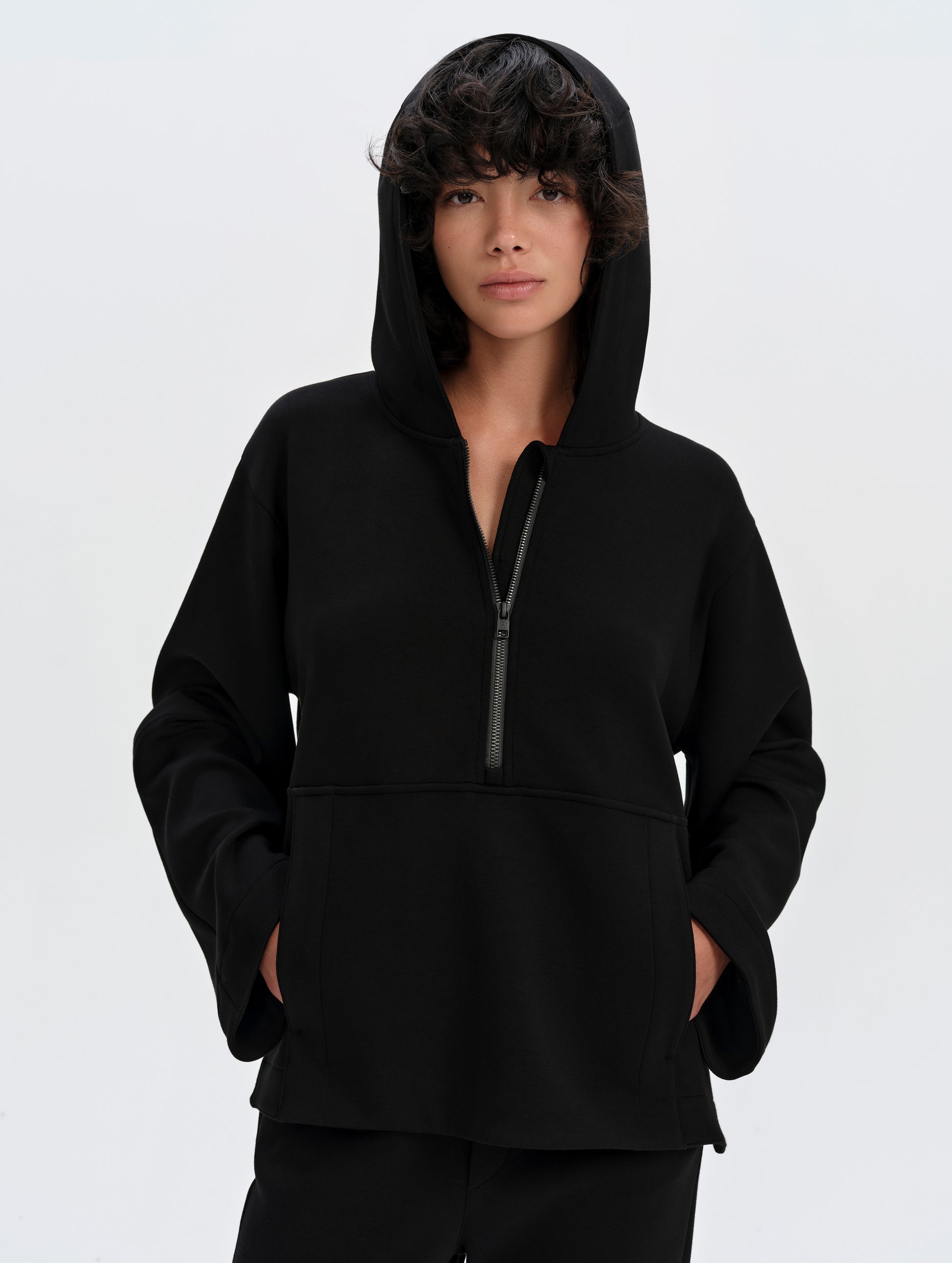 Front upper-body view of woman wearing the Blaire Premium Hoodie in Onyx Black from AETHER Apparel with the hood up. 