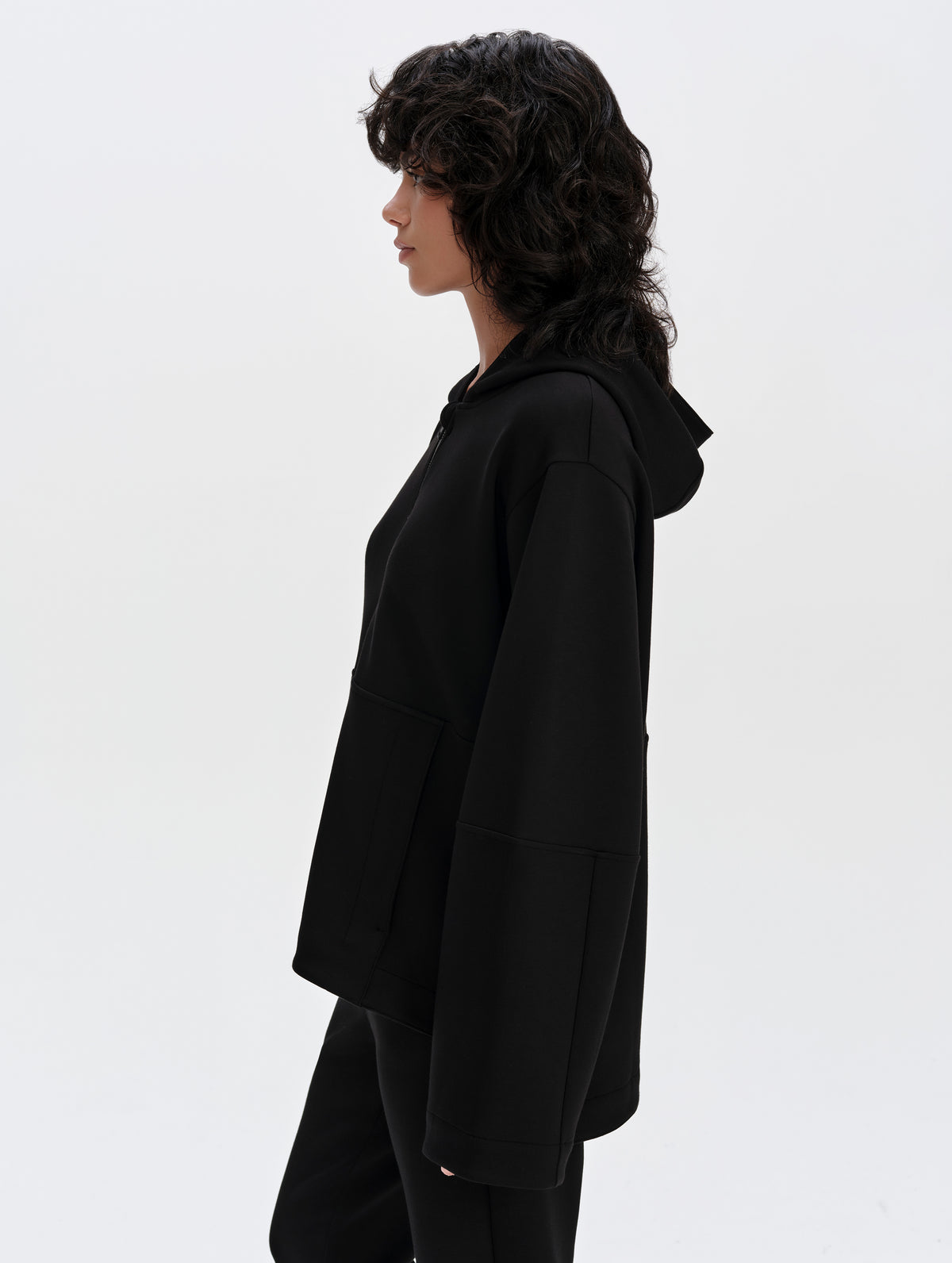 Side profile upper-body view of woman wearing the Blaire Premium Hoodie in Onyx Black from AETHER Apparel.