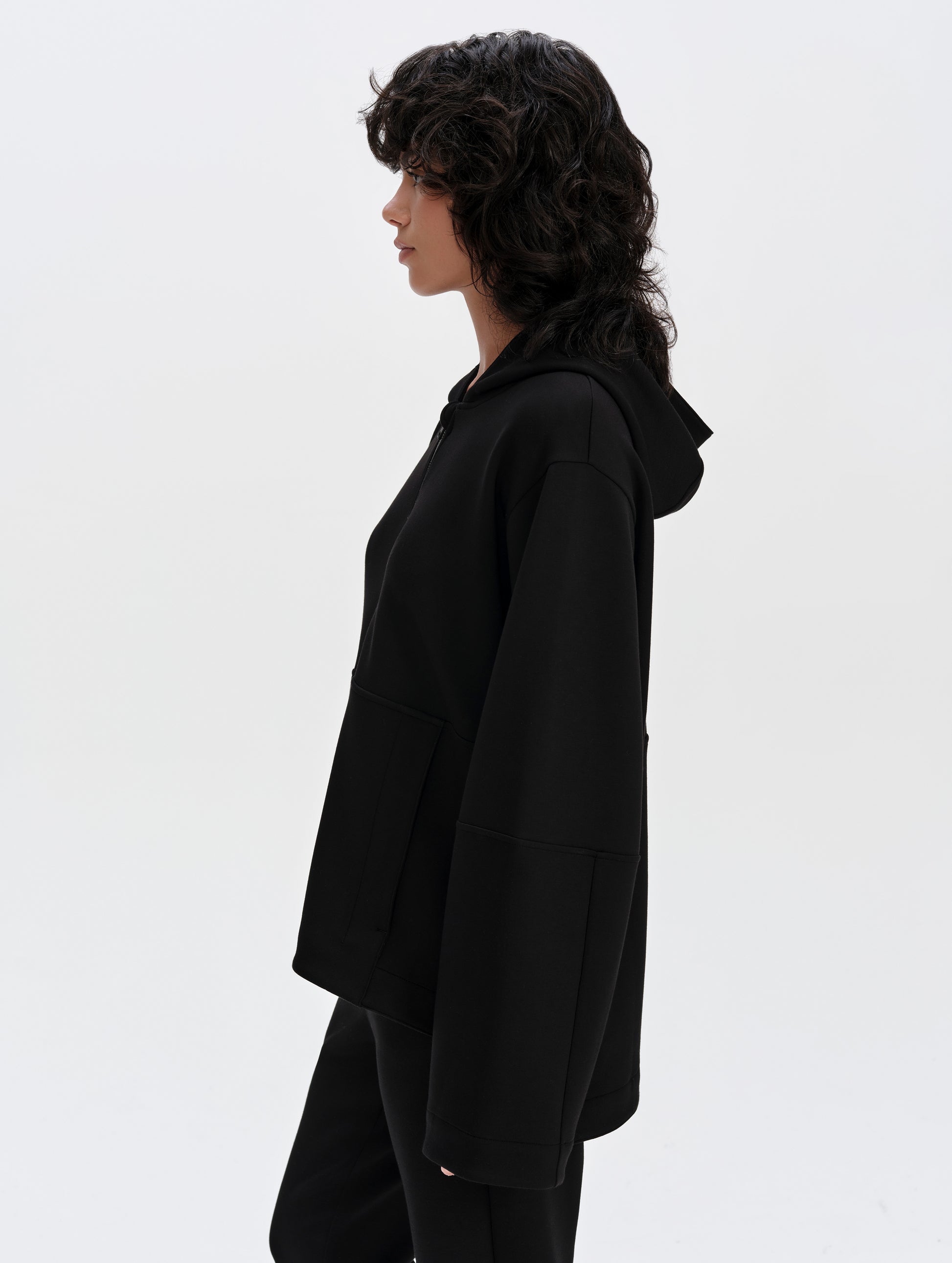 Side profile upper-body view of woman wearing the Blaire Premium Hoodie in Onyx Black from AETHER Apparel.