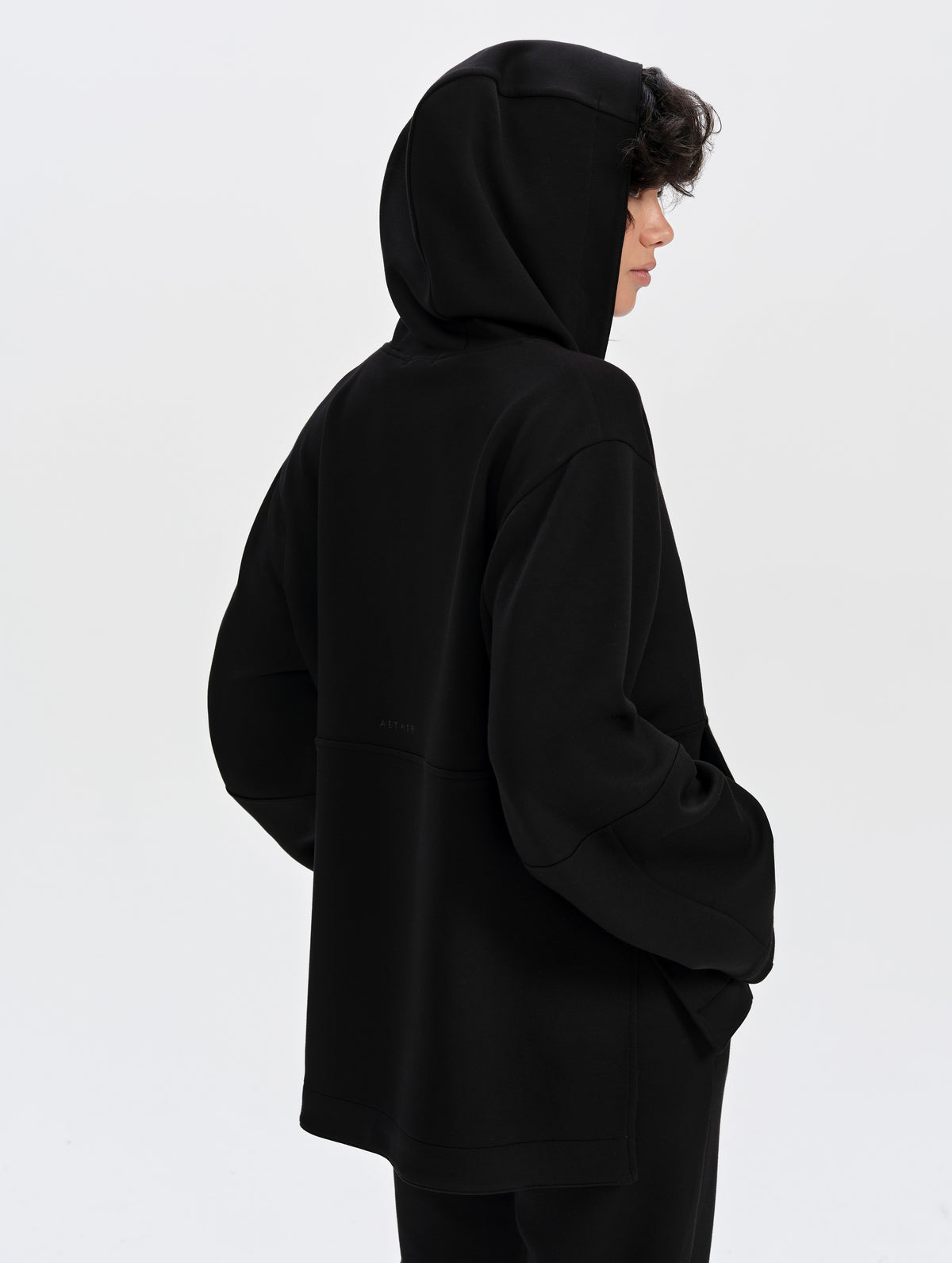 Rear 3/4 upper-body view of woman wearing the Blaire Premium Hoodie in Onyx Black from AETHER Apparel.