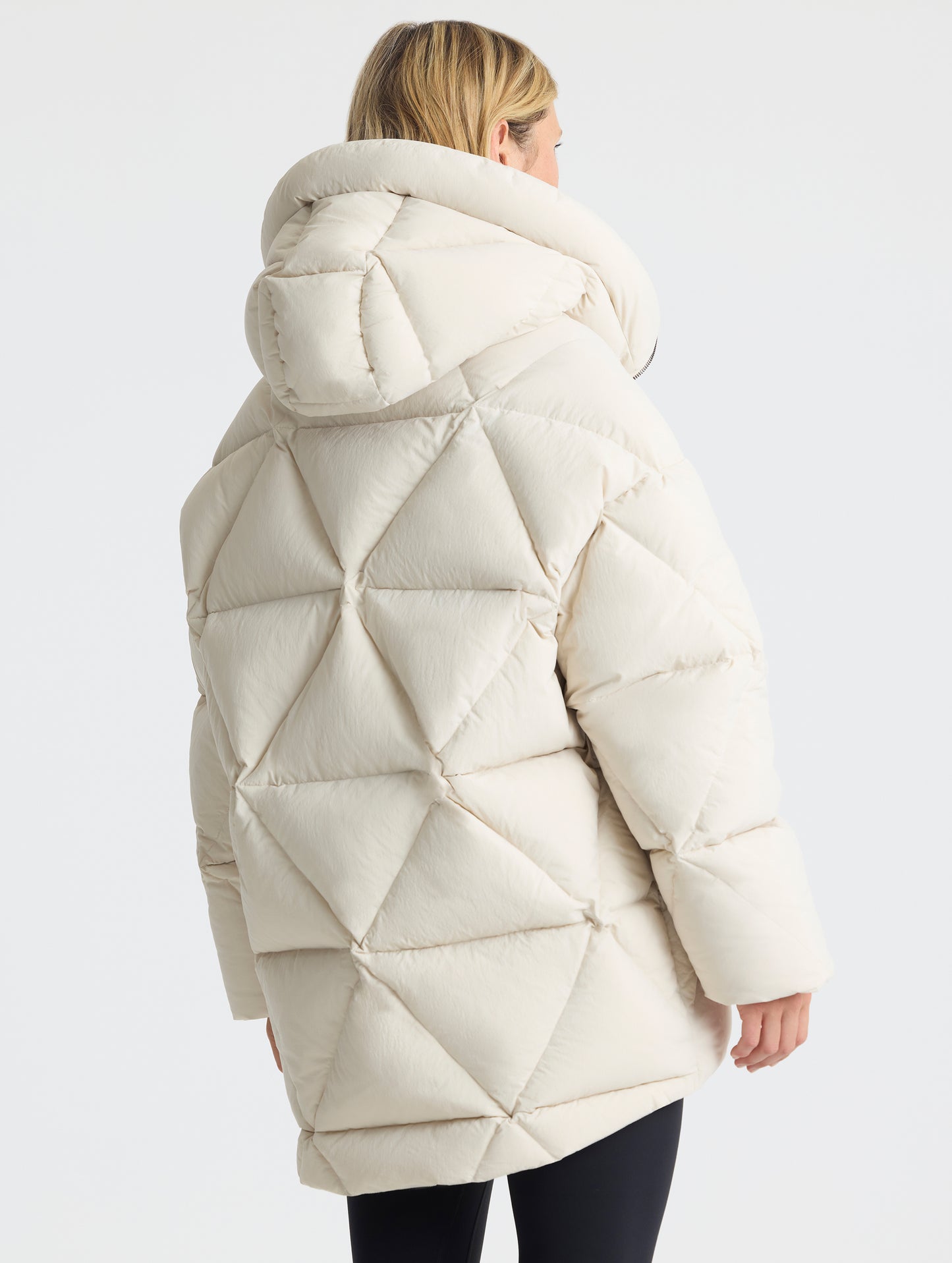 Rear angled upper-body view of woman wearing the Callie Oversized Down Parka in Bone from AETHER Apparel.