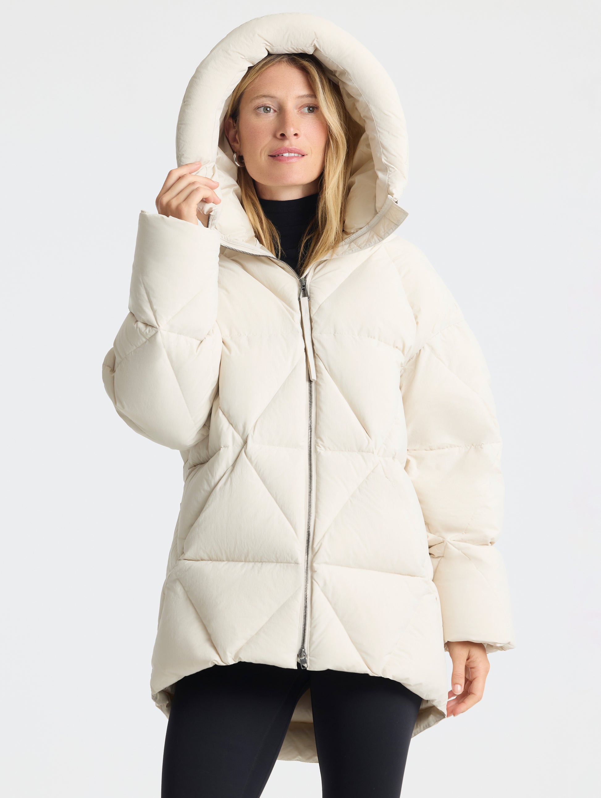 Front upper-body view of woman with hood up wearing the Callie Oversized Down Parka in Bone from AETHER Apparel.