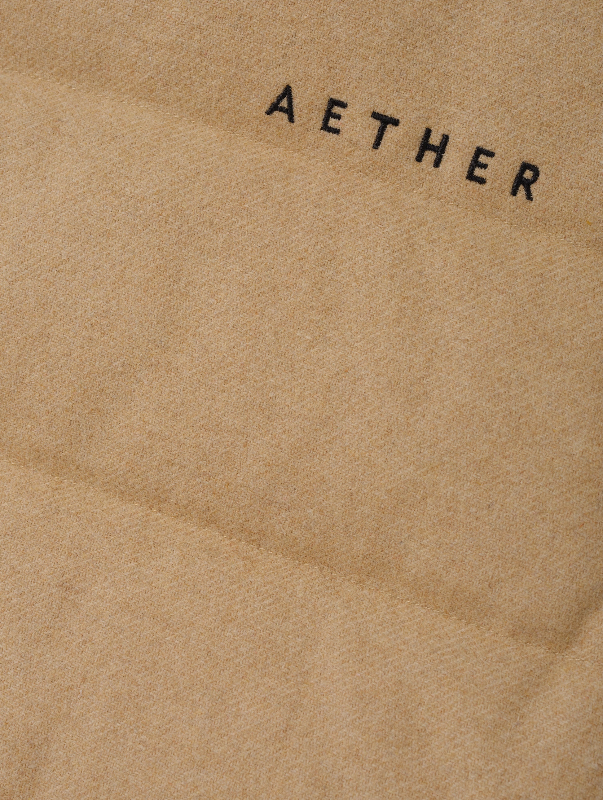 Closeup detailed view of the embroidered AETHER wordmark on the Channing Vest 2.0 in Latte Brown from AETHER Apparel.