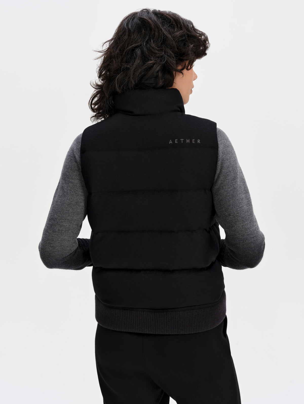 Rear upper-body view of woman wearing Channing Vest 2.0 in Onyx Black from AETHER Apparel.