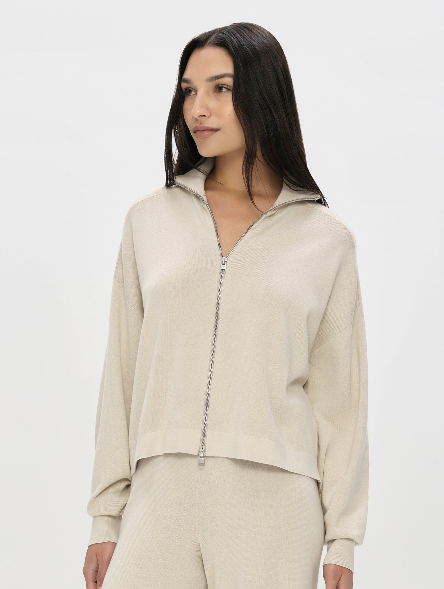 Front, upper-body view of woman wearing the Eliana Full-ZIp Sweater in Bone from AETHER Apparel.
