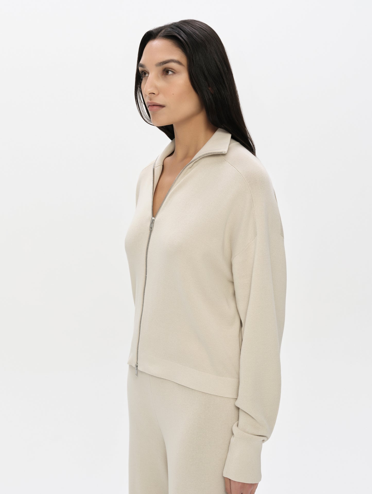 Front, 3/4, upper-body view of woman wearing the Eliana Full-ZIp Sweater in Bone from AETHER Apparel.