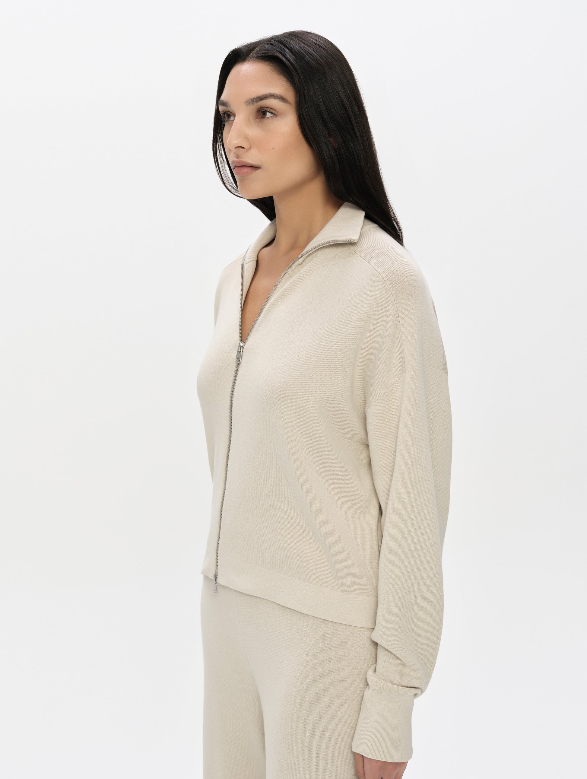 Front, 3/4, upper-body view of woman wearing the Eliana Full-ZIp Sweater in Bone from AETHER Apparel.