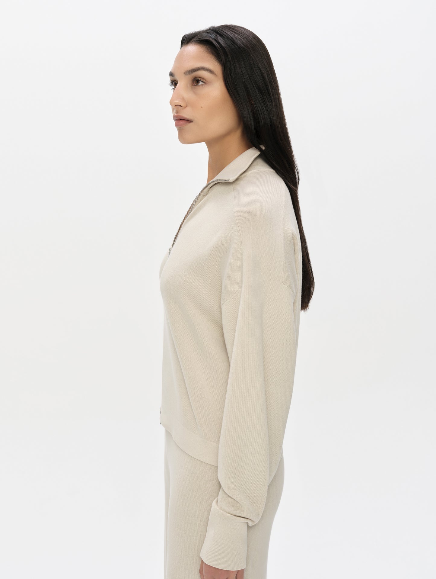 Side profile, upper-body view of woman wearing the Eliana Full-ZIp Sweater in Bone from AETHER Apparel.