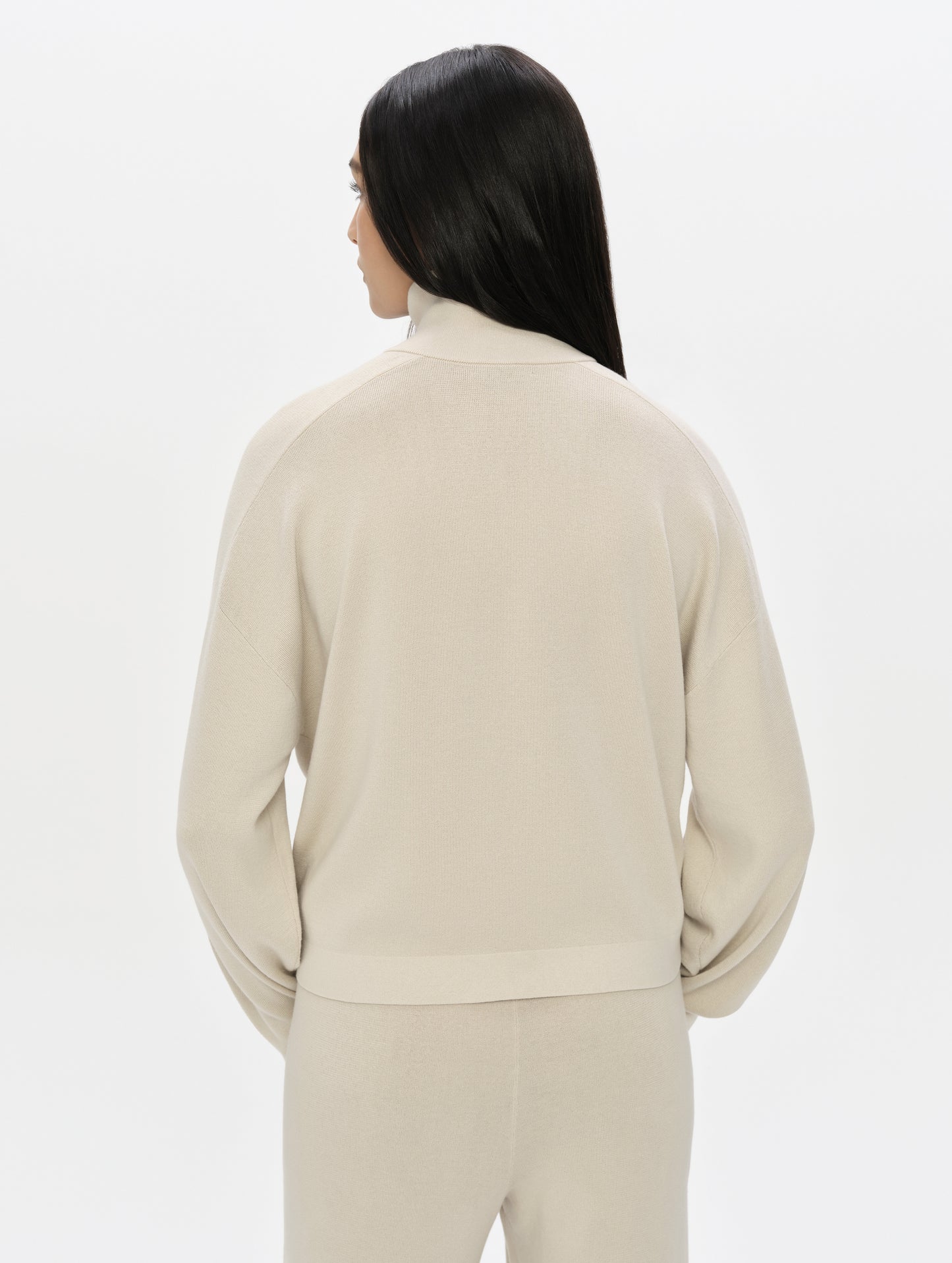 Rear, upper-body view of woman wearing the Eliana Full-ZIp Sweater in Bone from AETHER Apparel.