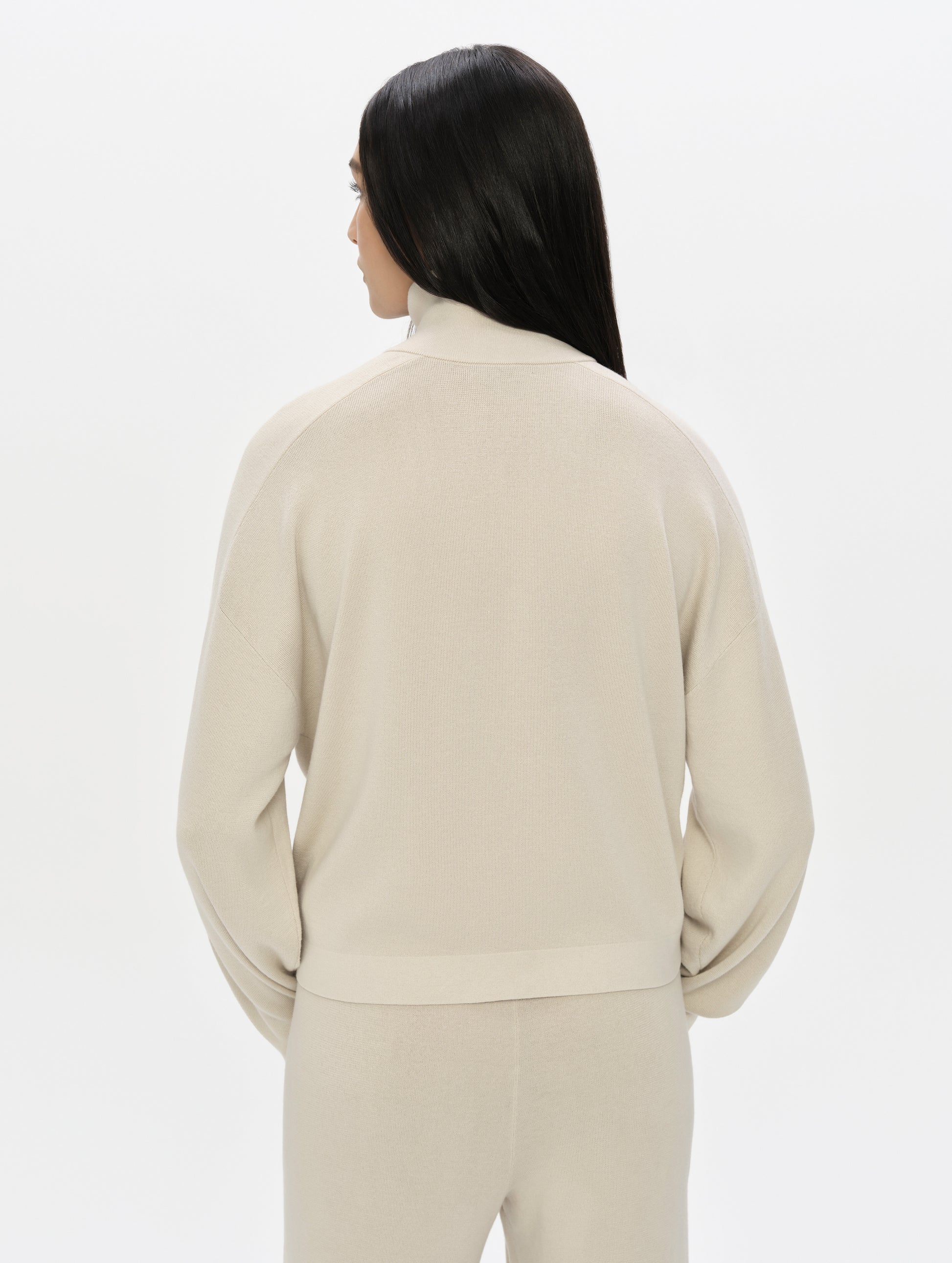 Rear, upper-body view of woman wearing the Eliana Full-ZIp Sweater in Bone from AETHER Apparel.