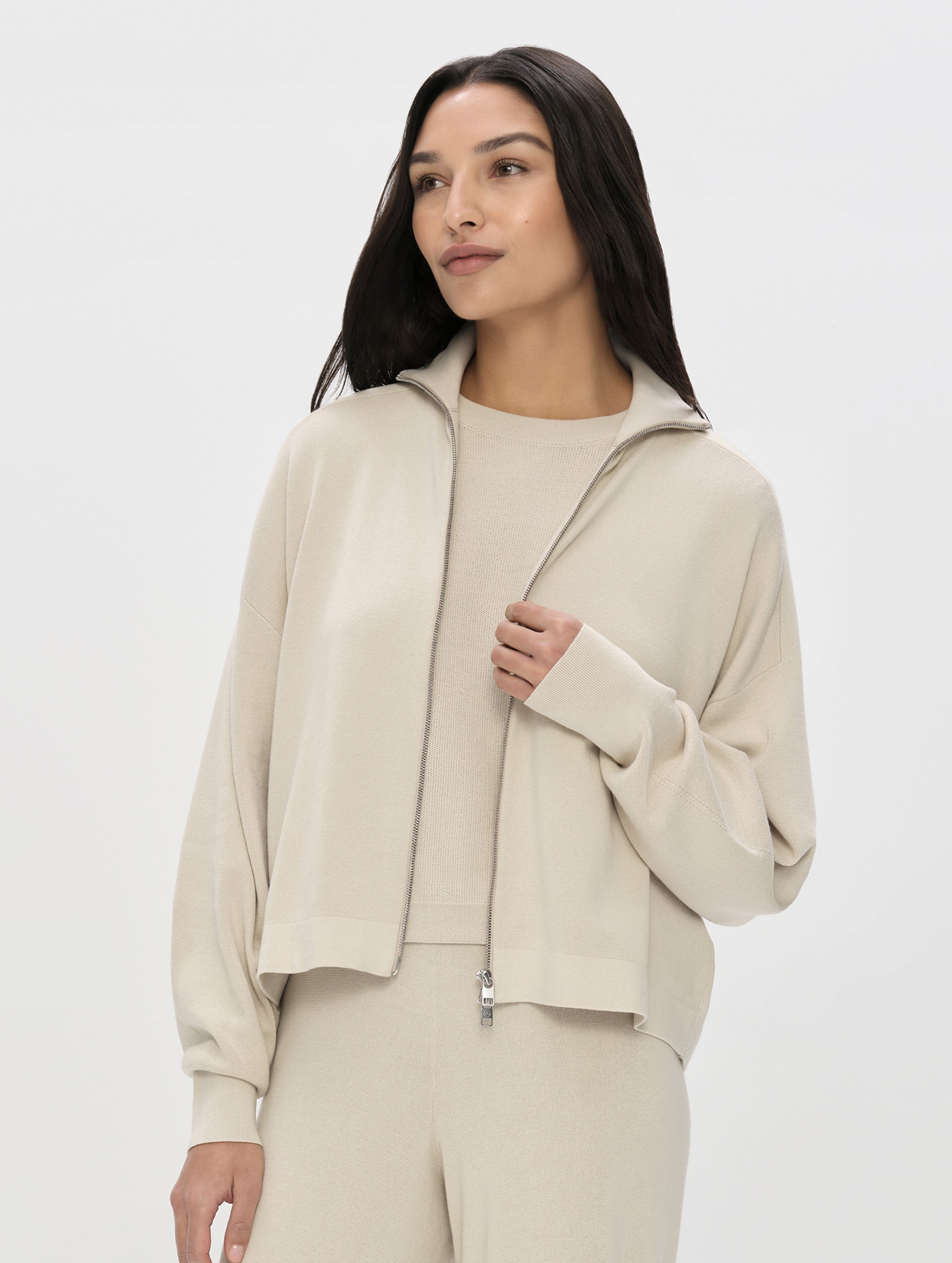 Front, upper-body view of woman wearing the Eliana Full-ZIp Sweater in Bone from AETHER Apparel unzipped. 