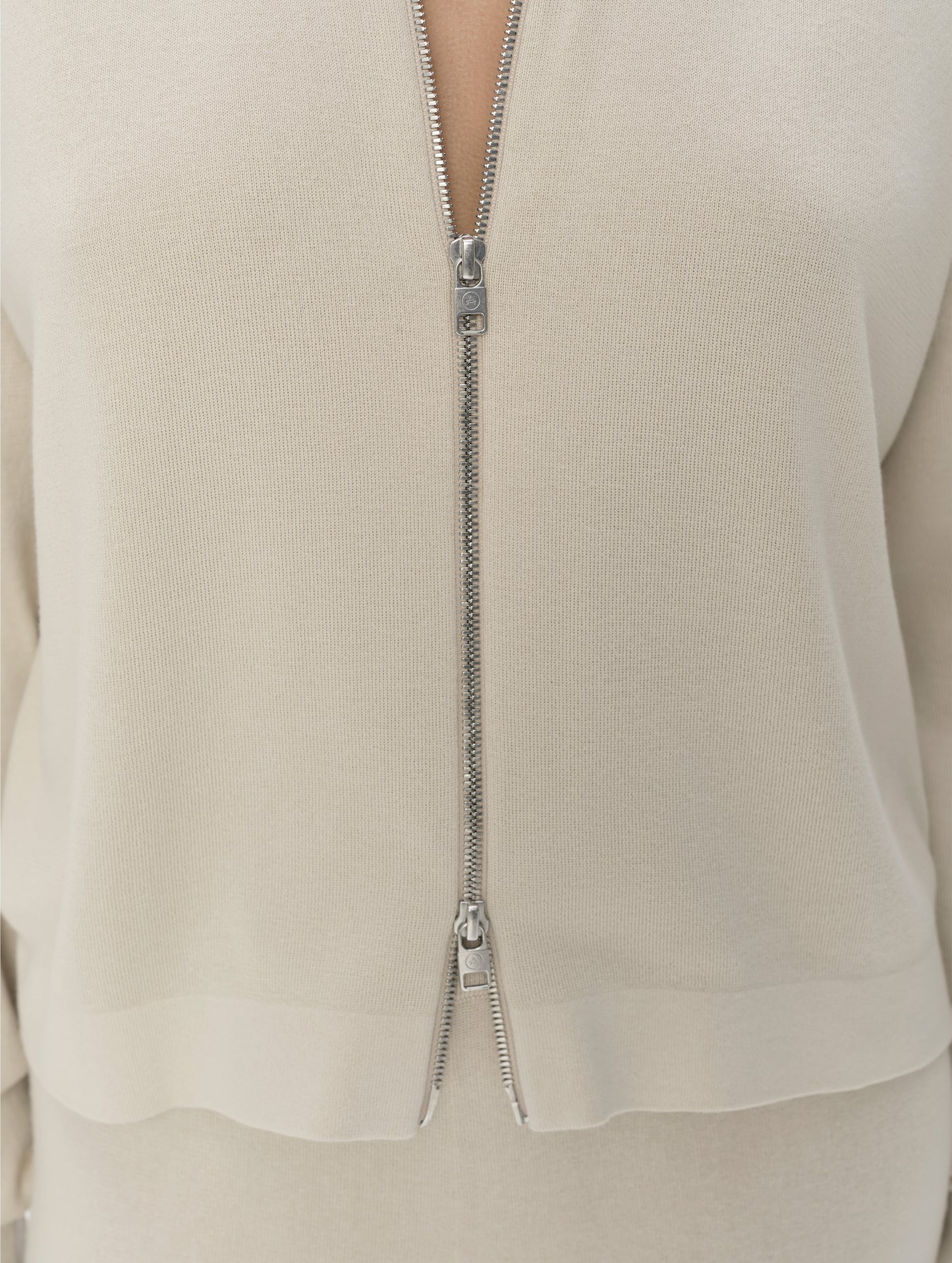 Closeup detailed view of the main center-front two-way zipper on the Eliana Full-ZIp Sweater in Bone from AETHER Apparel.
