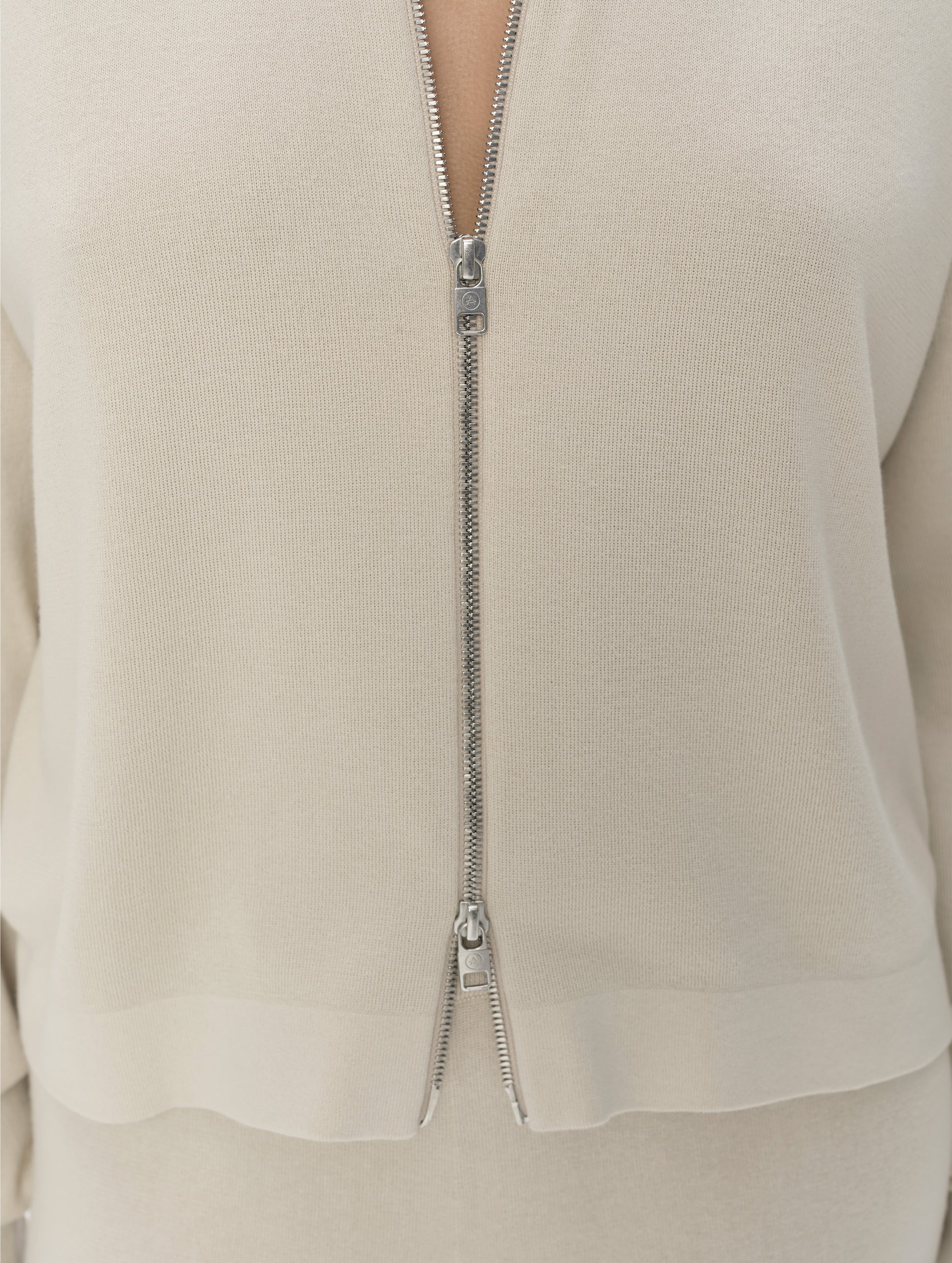 Closeup detailed view of the main center-front two-way zipper on the Eliana Full-ZIp Sweater in Bone from AETHER Apparel.