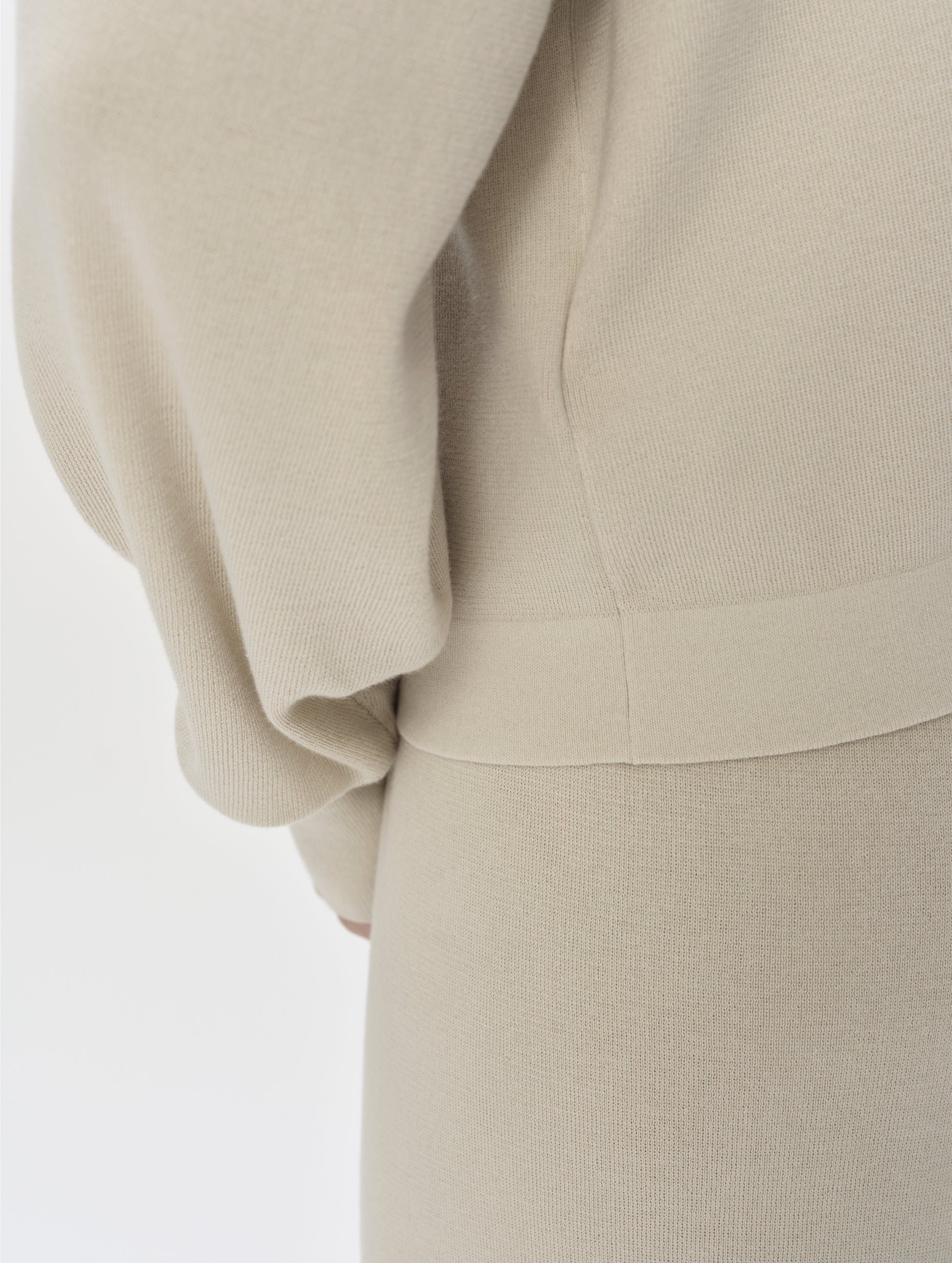 Closeup detailed view of the bottom hem on the Eliana Full-ZIp Sweater in Bone from AETHER Apparel.