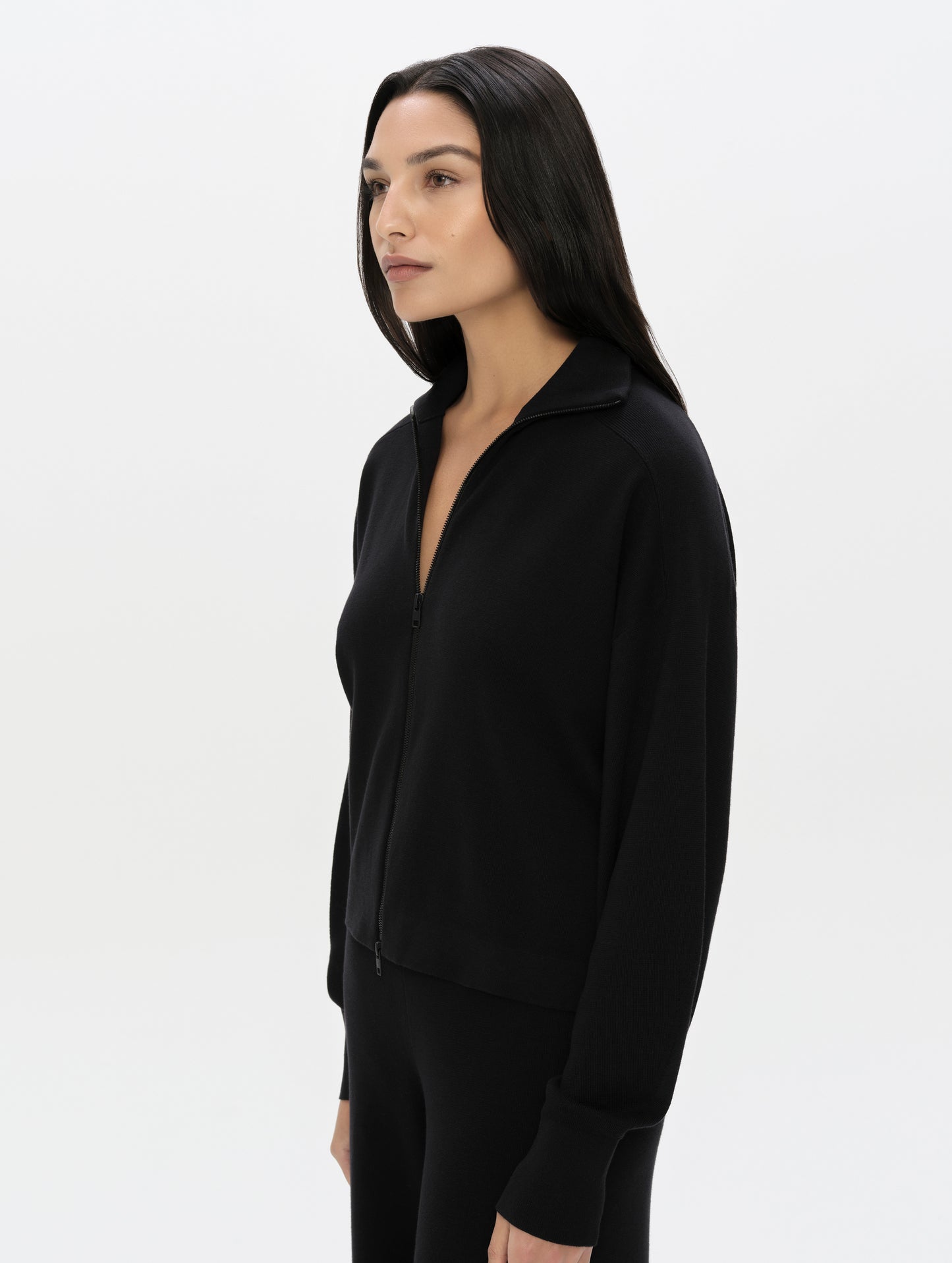 Front, 3/4, upper-body view of woman wearing the Eliana Full-ZIp Sweater in Onyx Black from AETHER Apparel.