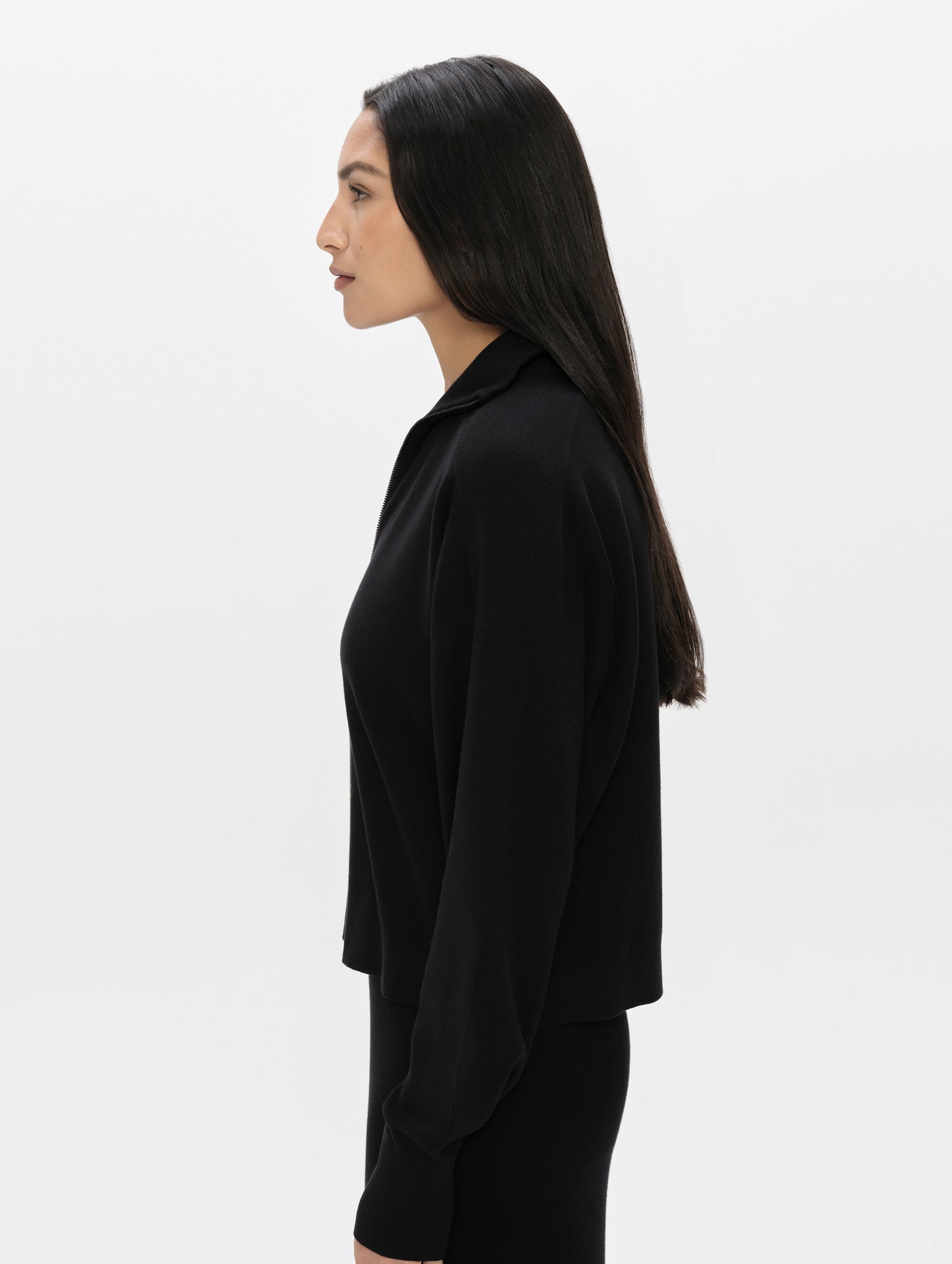Side profile, upper-body view of woman wearing the Eliana Full-ZIp Sweater in Onyx Black from AETHER Apparel.