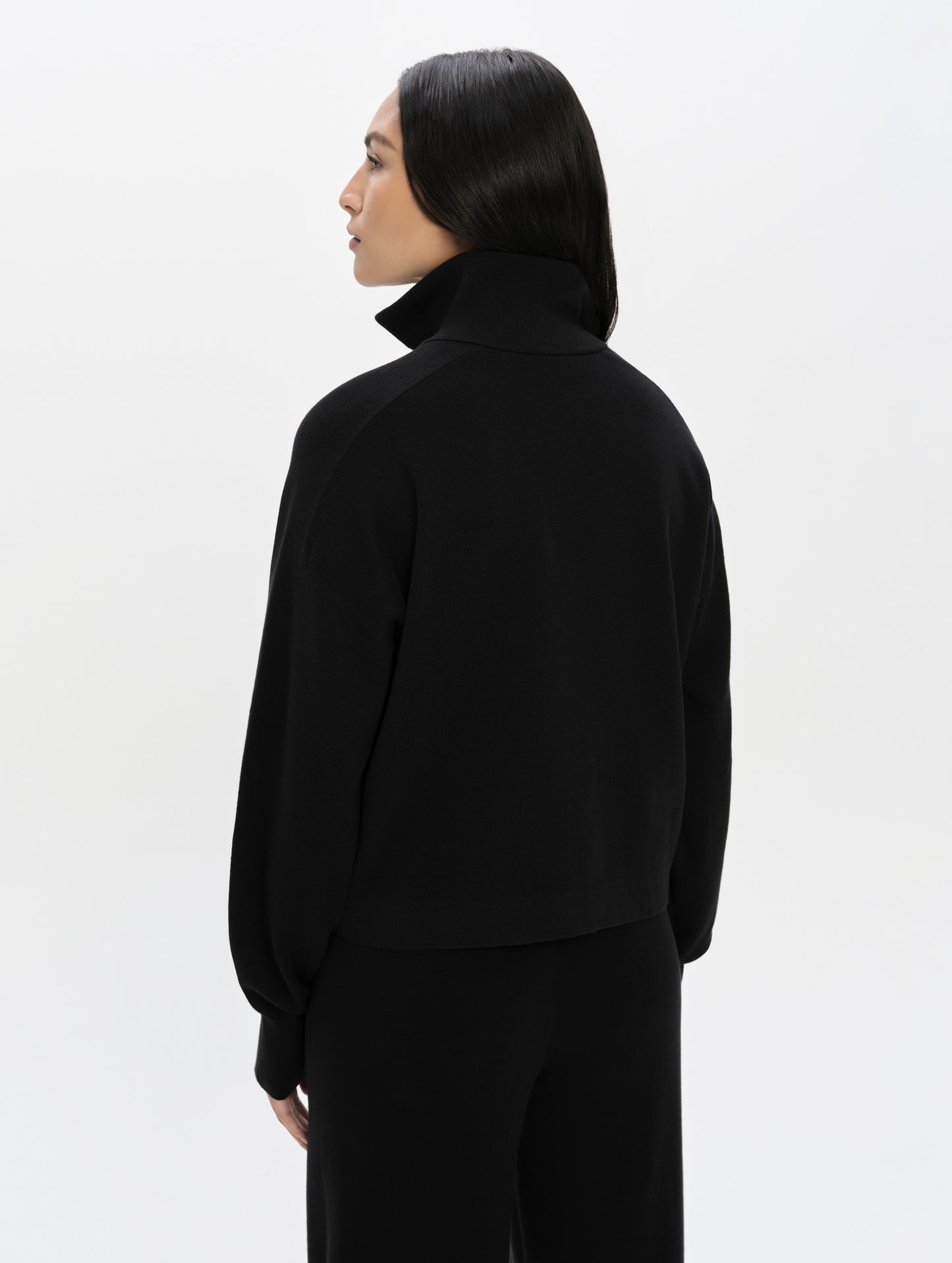 Rear, upper-body view of woman wearing the Eliana Full-ZIp Sweater in Onyx Black from AETHER Apparel.