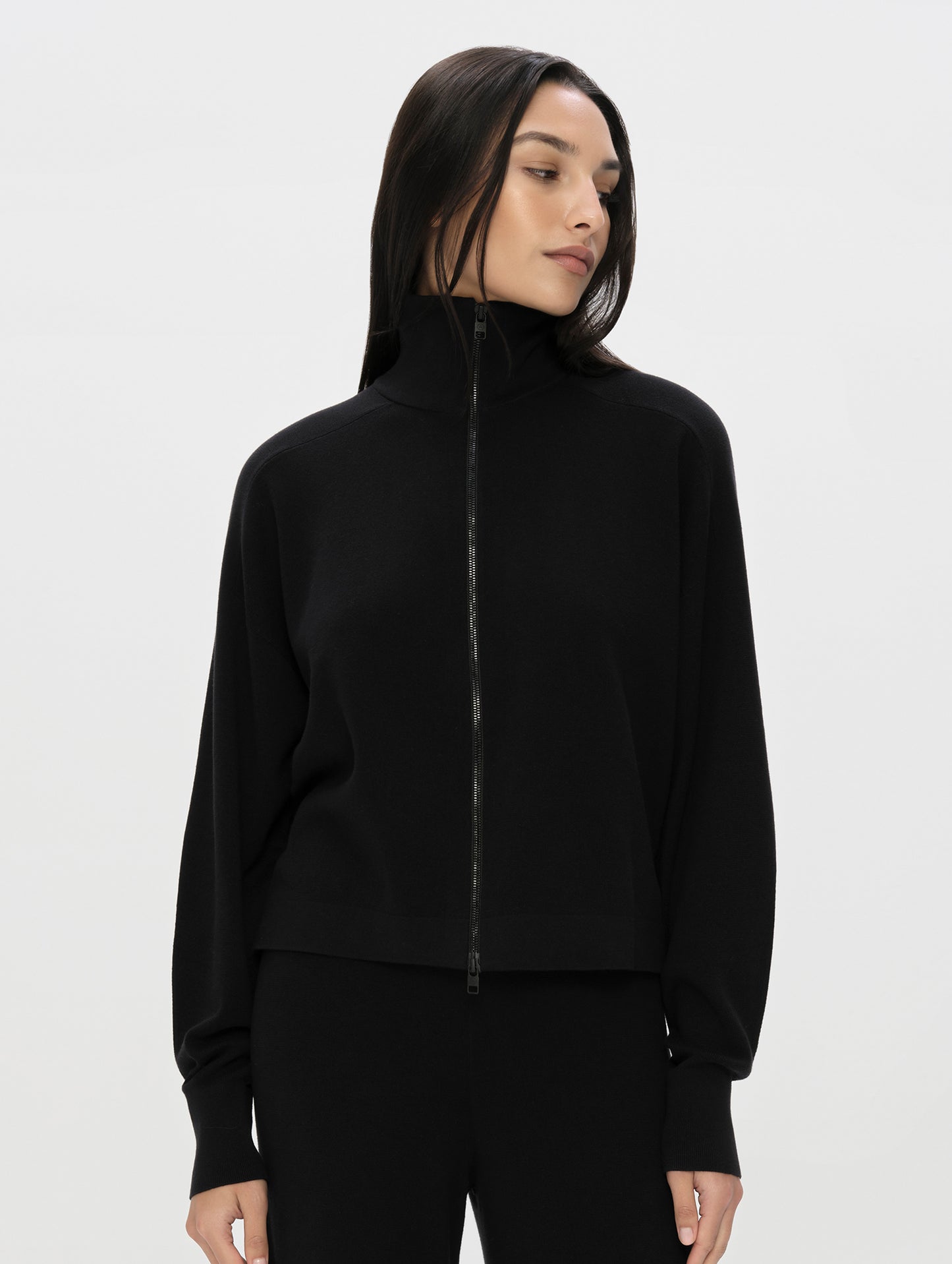Front, upper-body view of woman wearing the Eliana Full-ZIp Sweater in Onyx Black from AETHER Apparel zipped up.