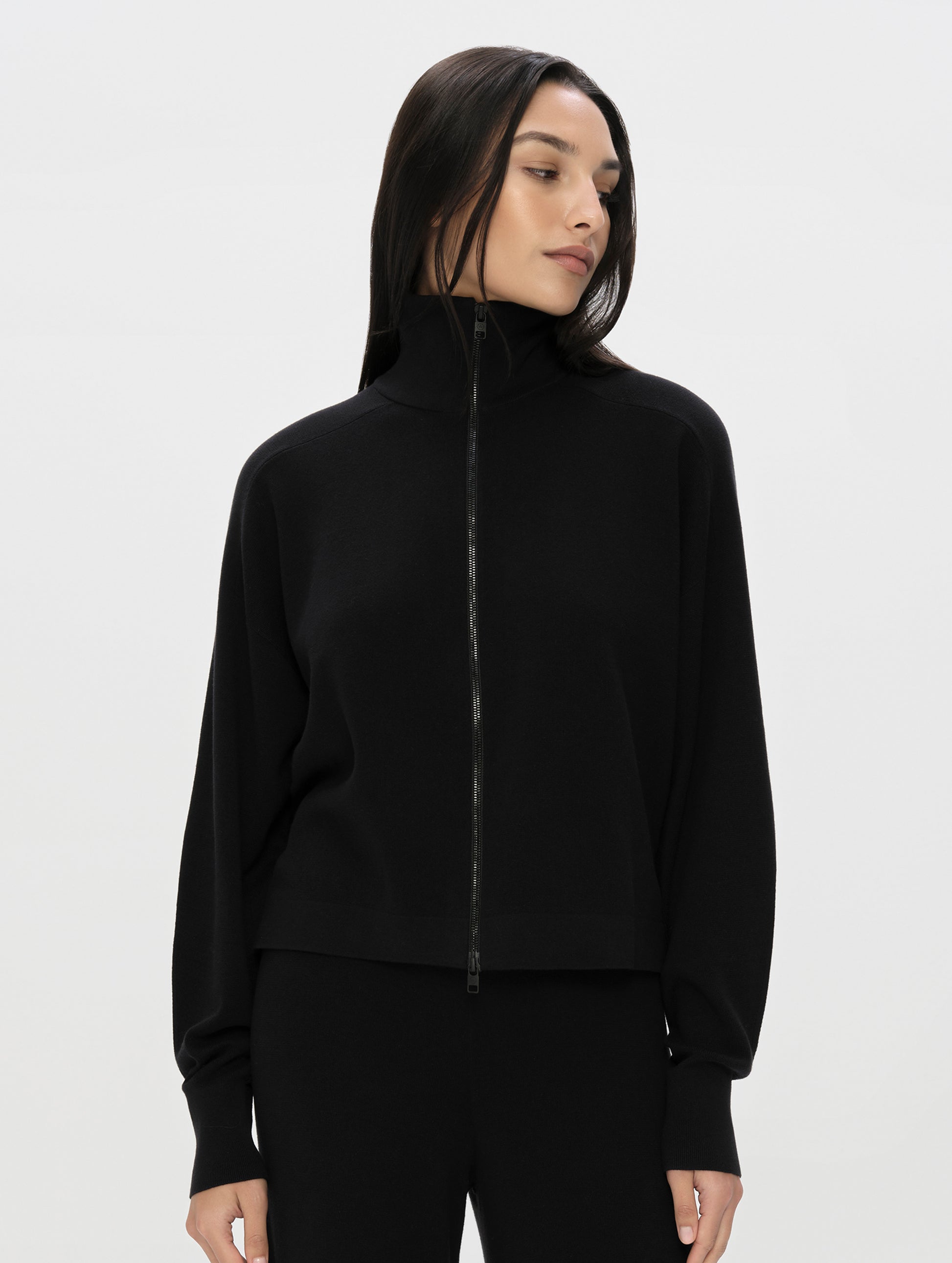 Front, upper-body view of woman wearing the Eliana Full-ZIp Sweater in Onyx Black from AETHER Apparel zipped up.