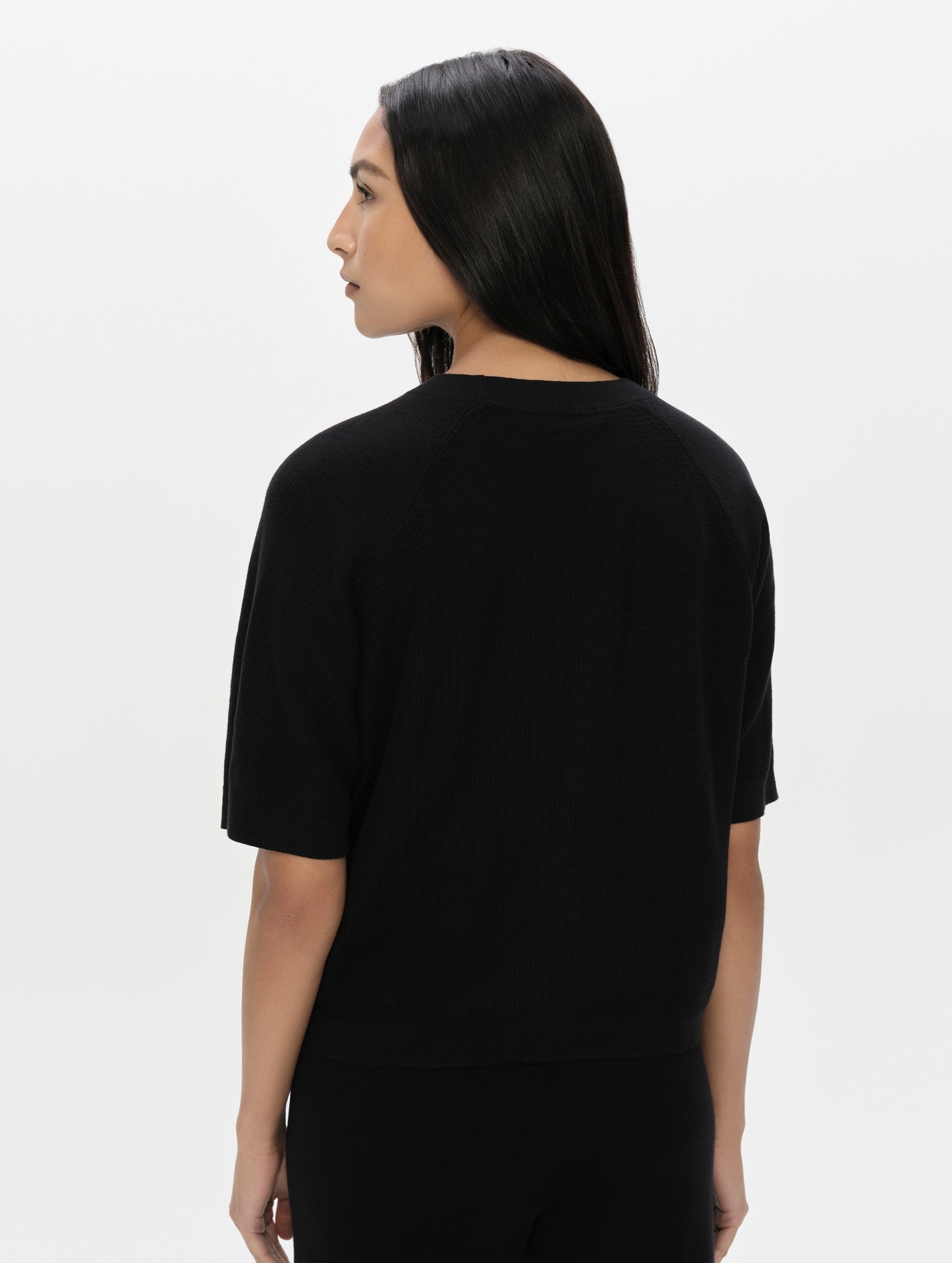 Rear, upper-body view of woman wearing the Eliana Sweater Tee in Onyx Black from AETHER Apparel.