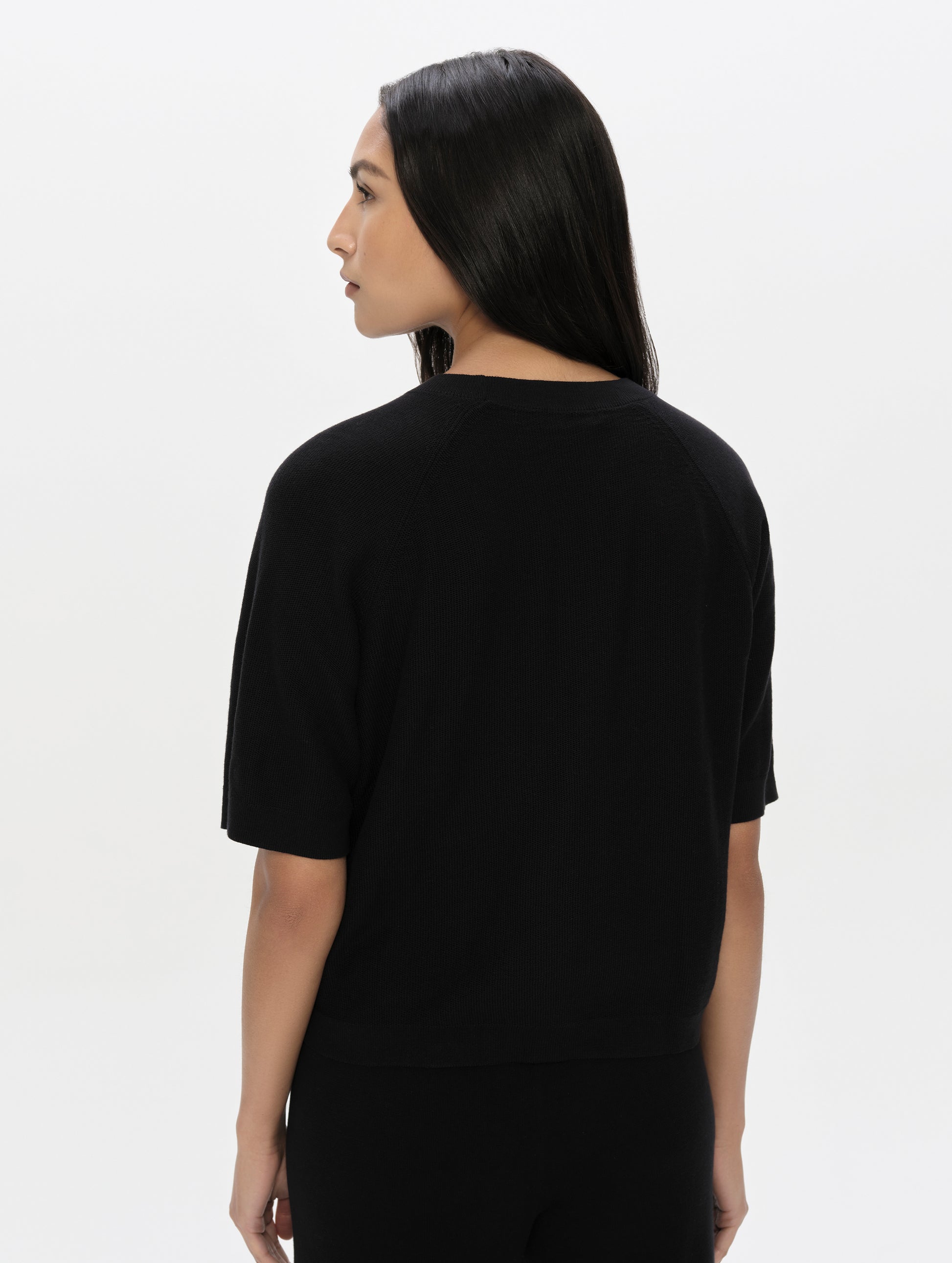 Rear, upper-body view of woman wearing the Eliana Sweater Tee in Onyx Black from AETHER Apparel.
