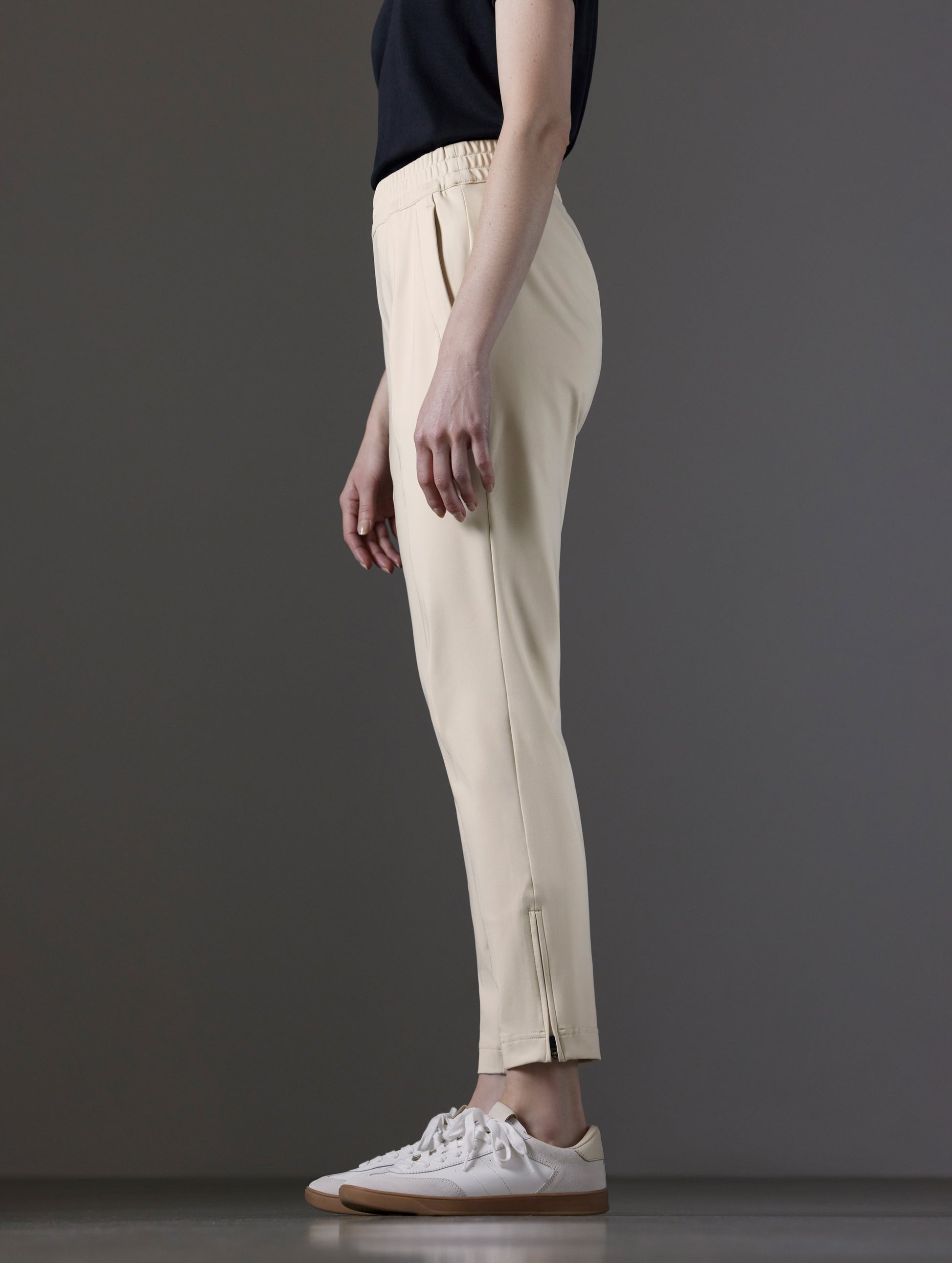 Side profile lower body view of woman wearing Eloise Travel Slim Pant in Bone white from AETHER Apparel.