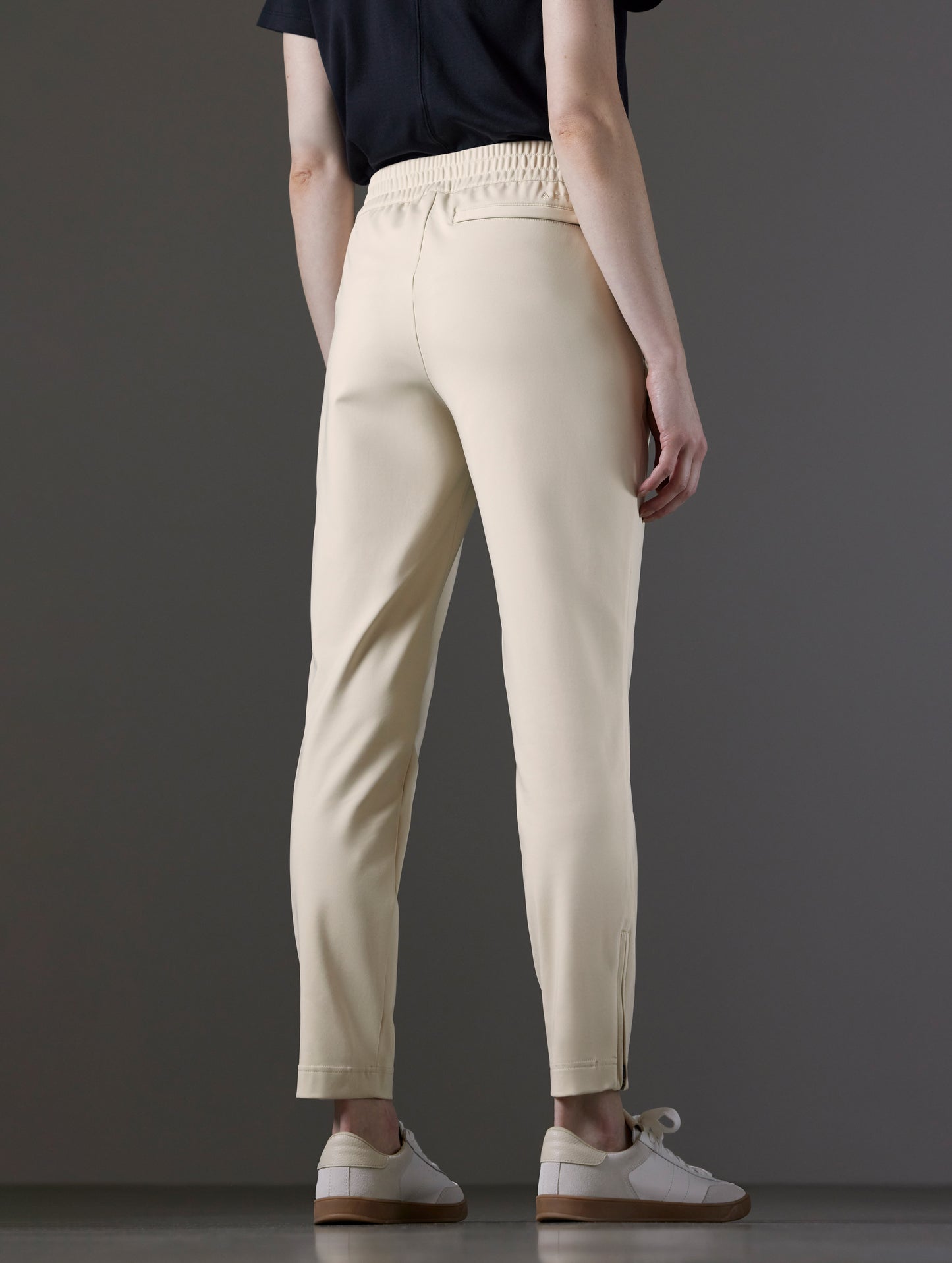 Rear angled lower body view of woman wearing Eloise Travel Slim Pant in Bone white from AETHER Apparel.